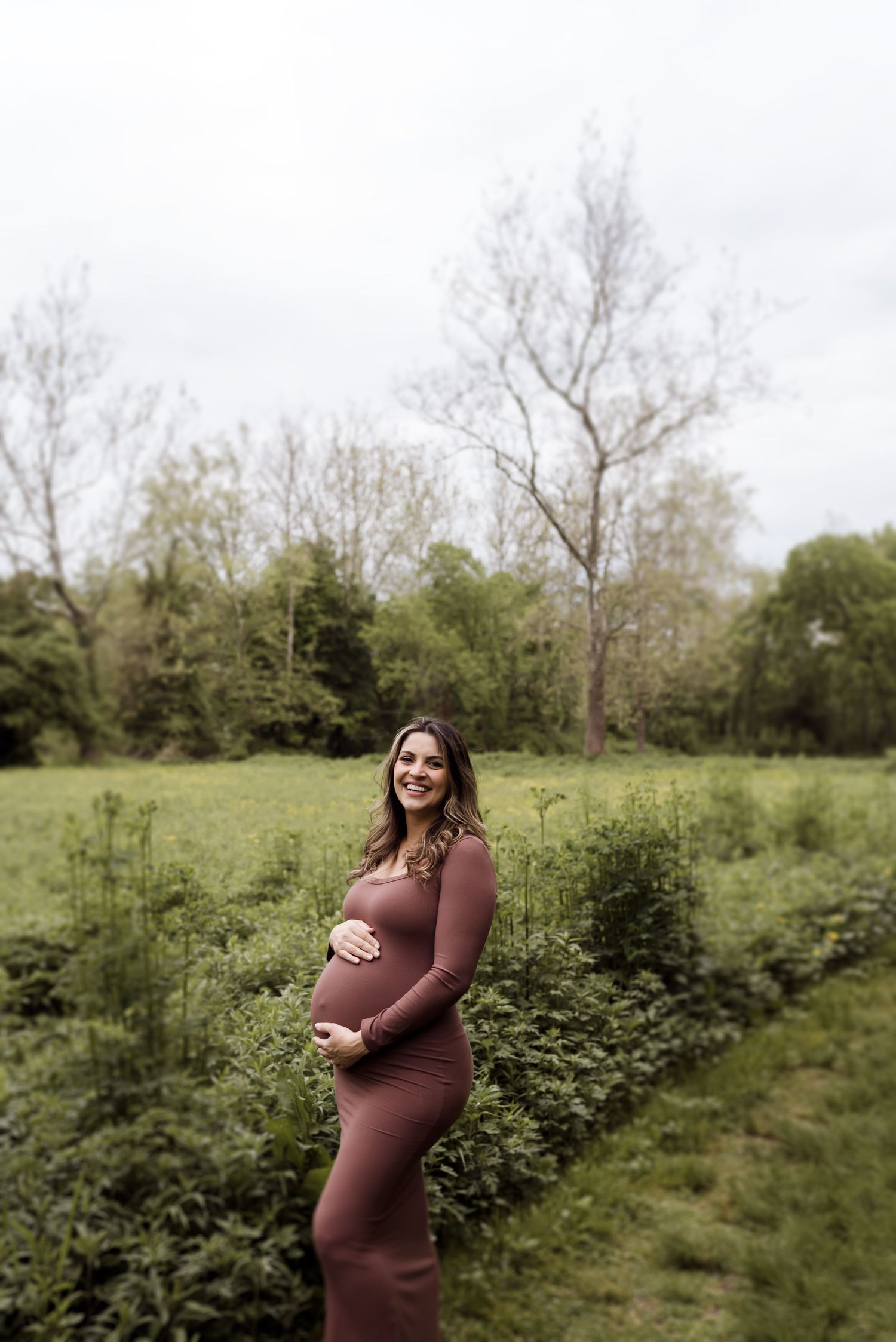A maternity portrait session in a rustic outdoor setting with natural greenery.