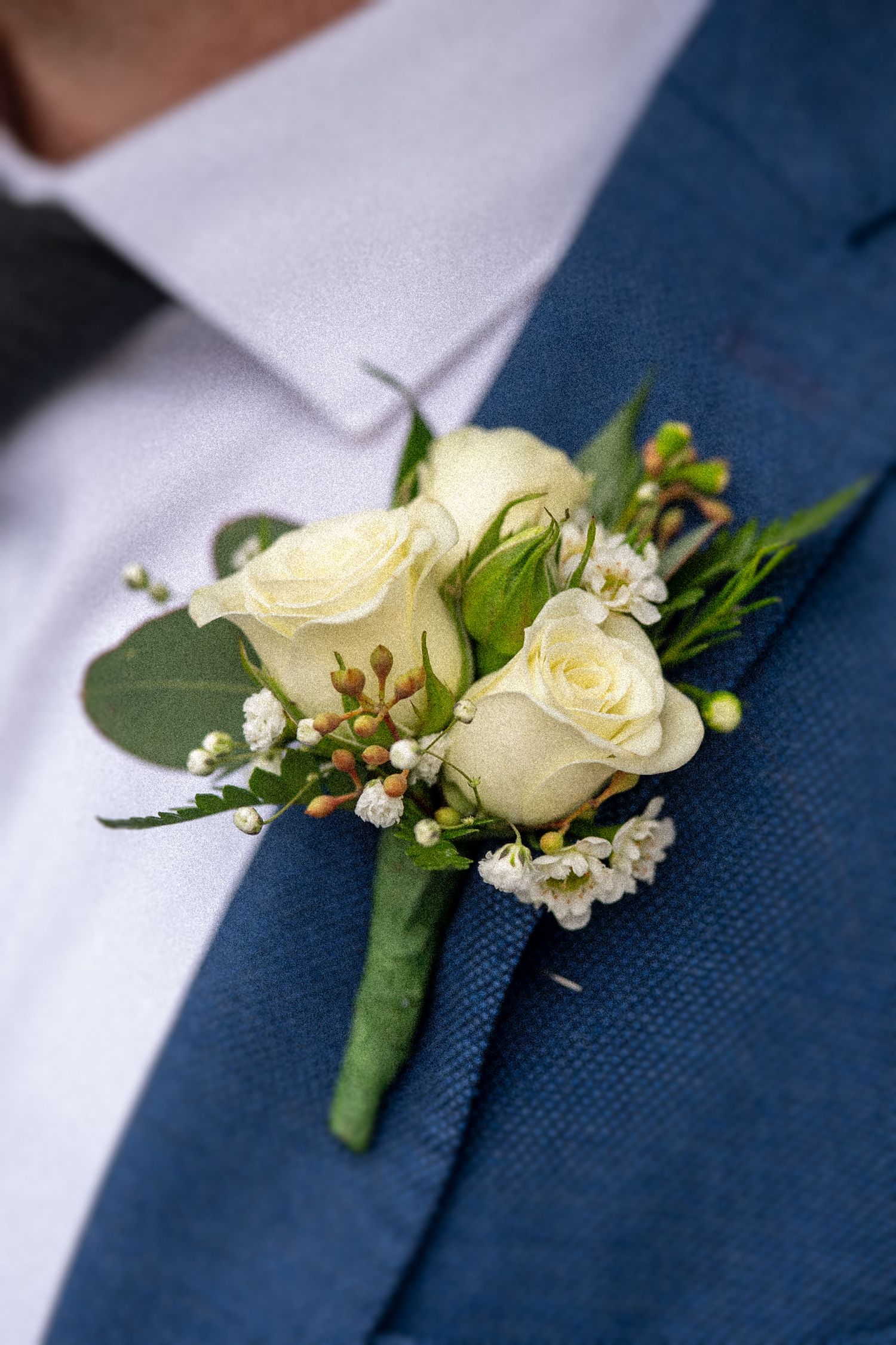 Elegant white rose and baby's breath boutonniere pinned to a navy blue suit jacket.