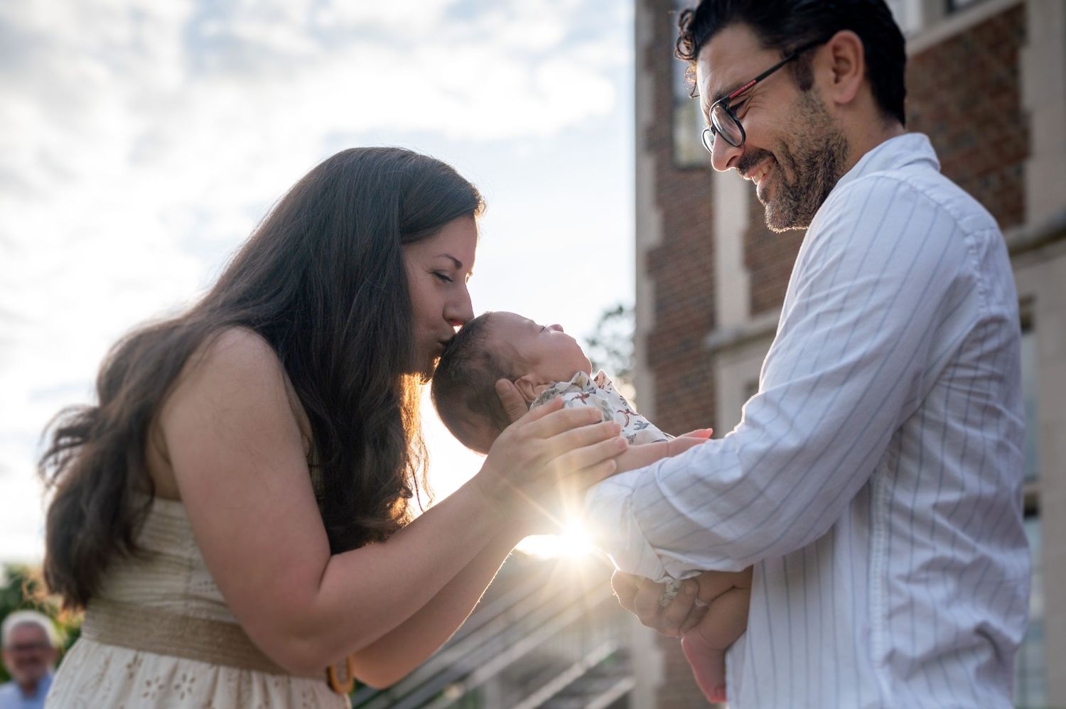 Tender family moment captured in warm sunlight against cloudy sky.