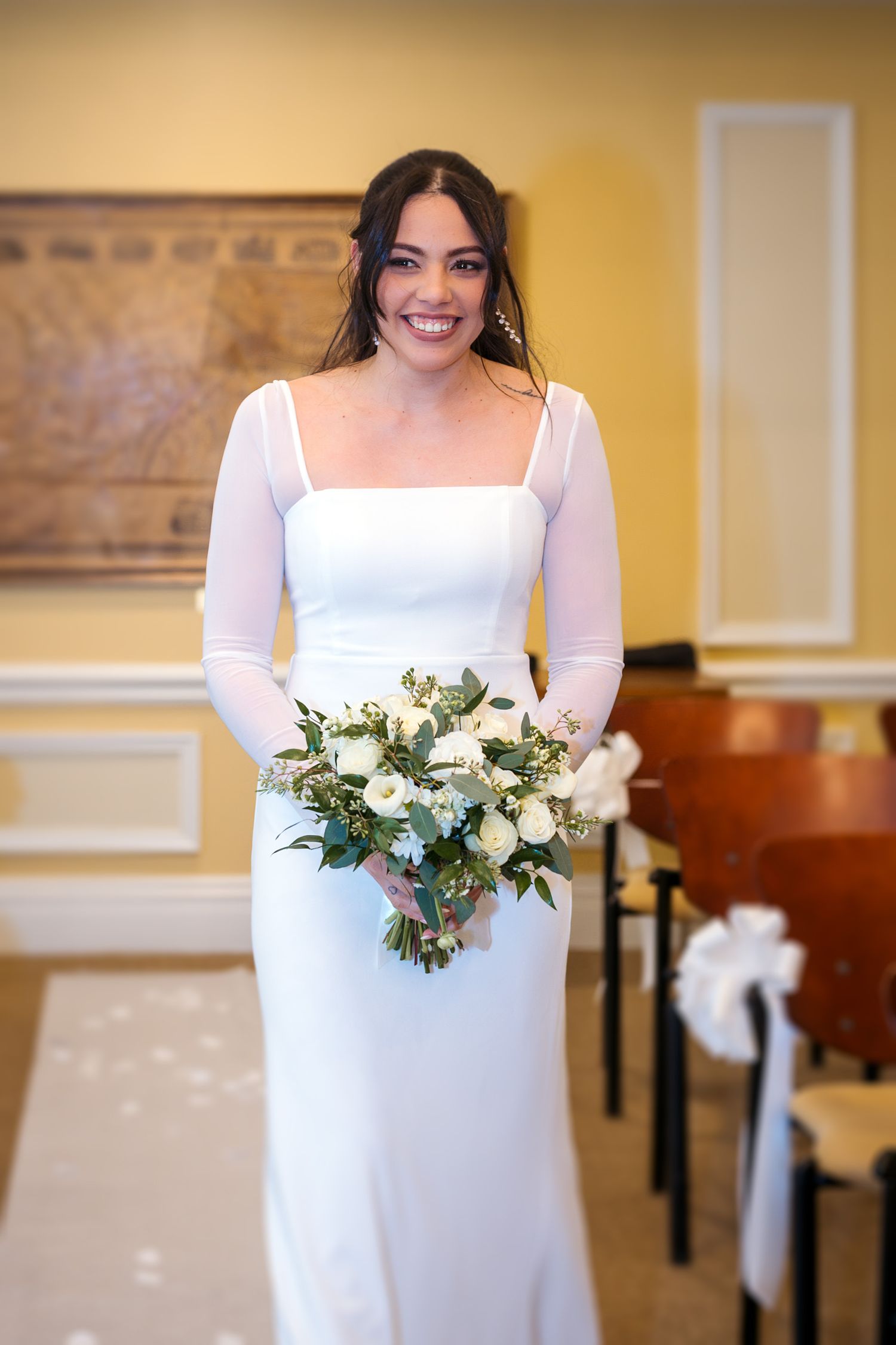Wedding bouquet with white flowers and greenery against a yellow wall.