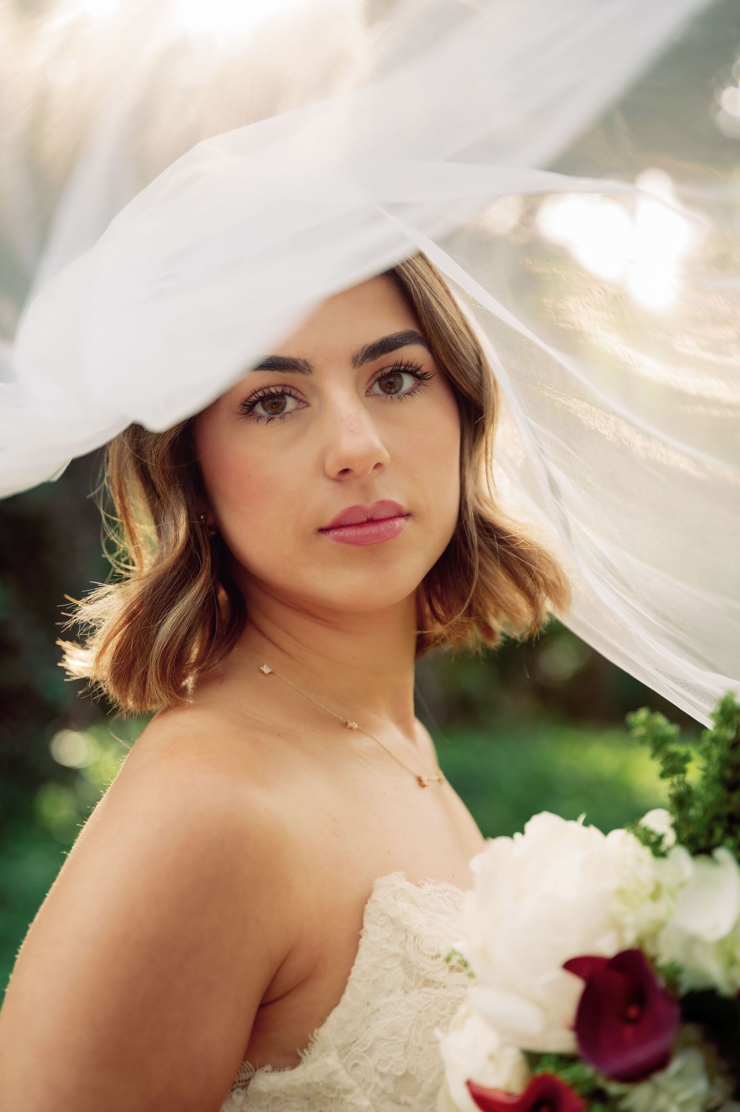Close-up bridal portrait with delicate veil and soft lighting in an outdoor garden setting.