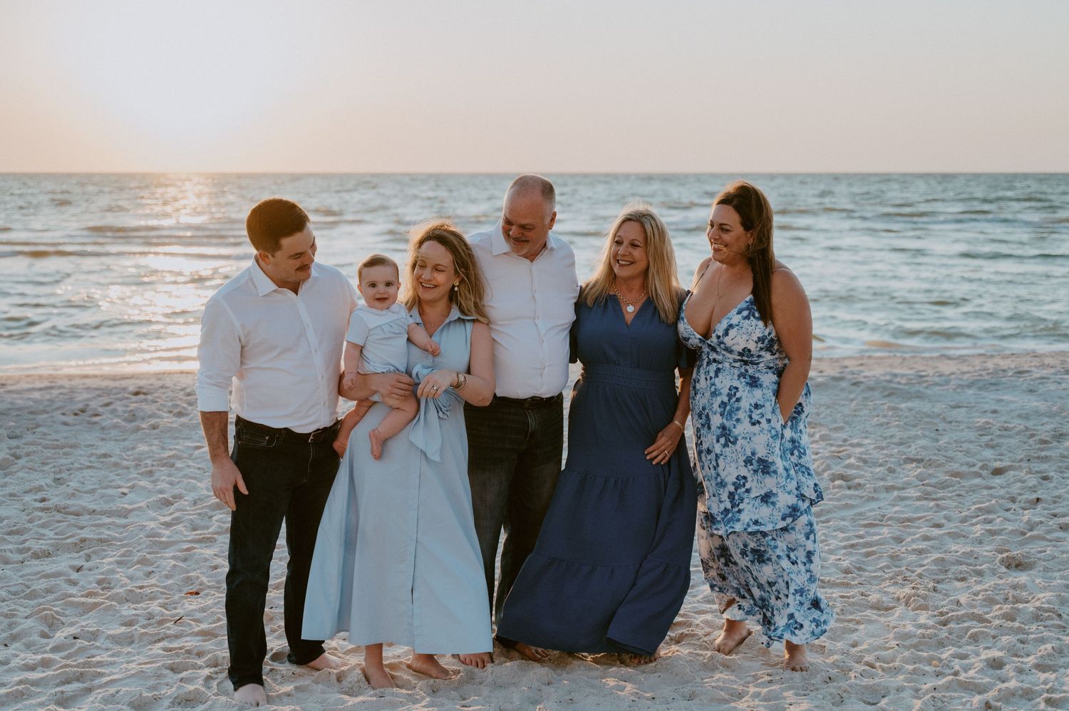 Family enjoying a sunset photoshoot together on a sandy beach with ocean waves in the background.