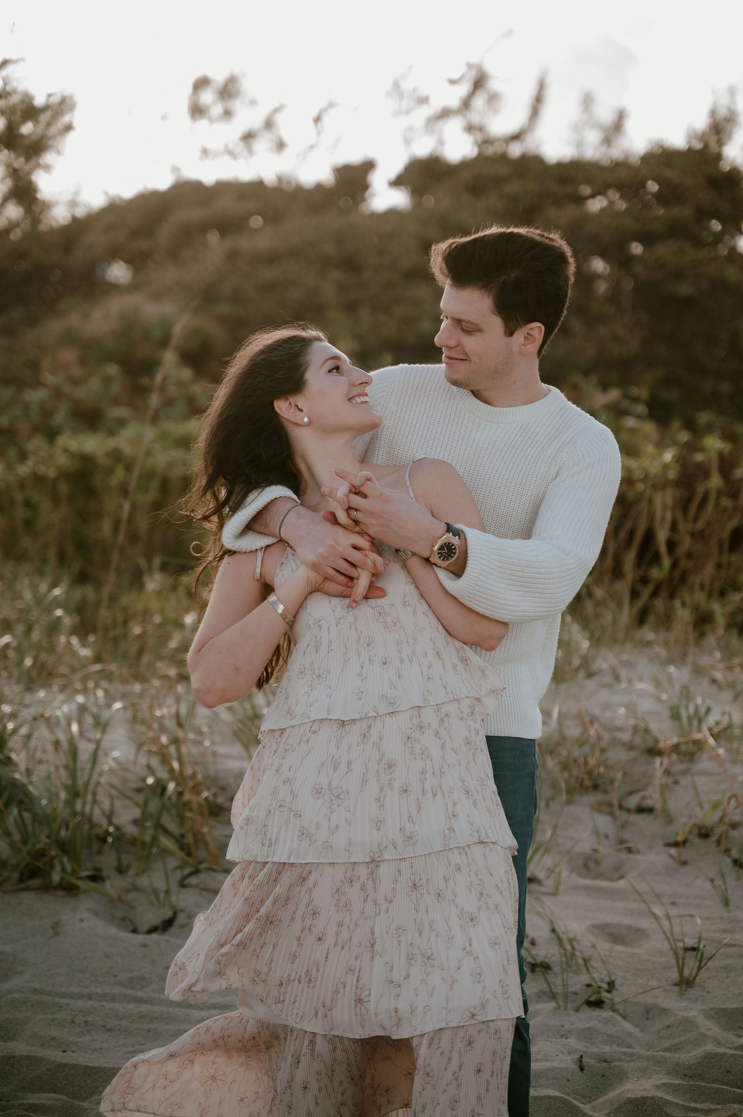 Romantic couple embracing and laughing together on sandy dunes during golden hour.