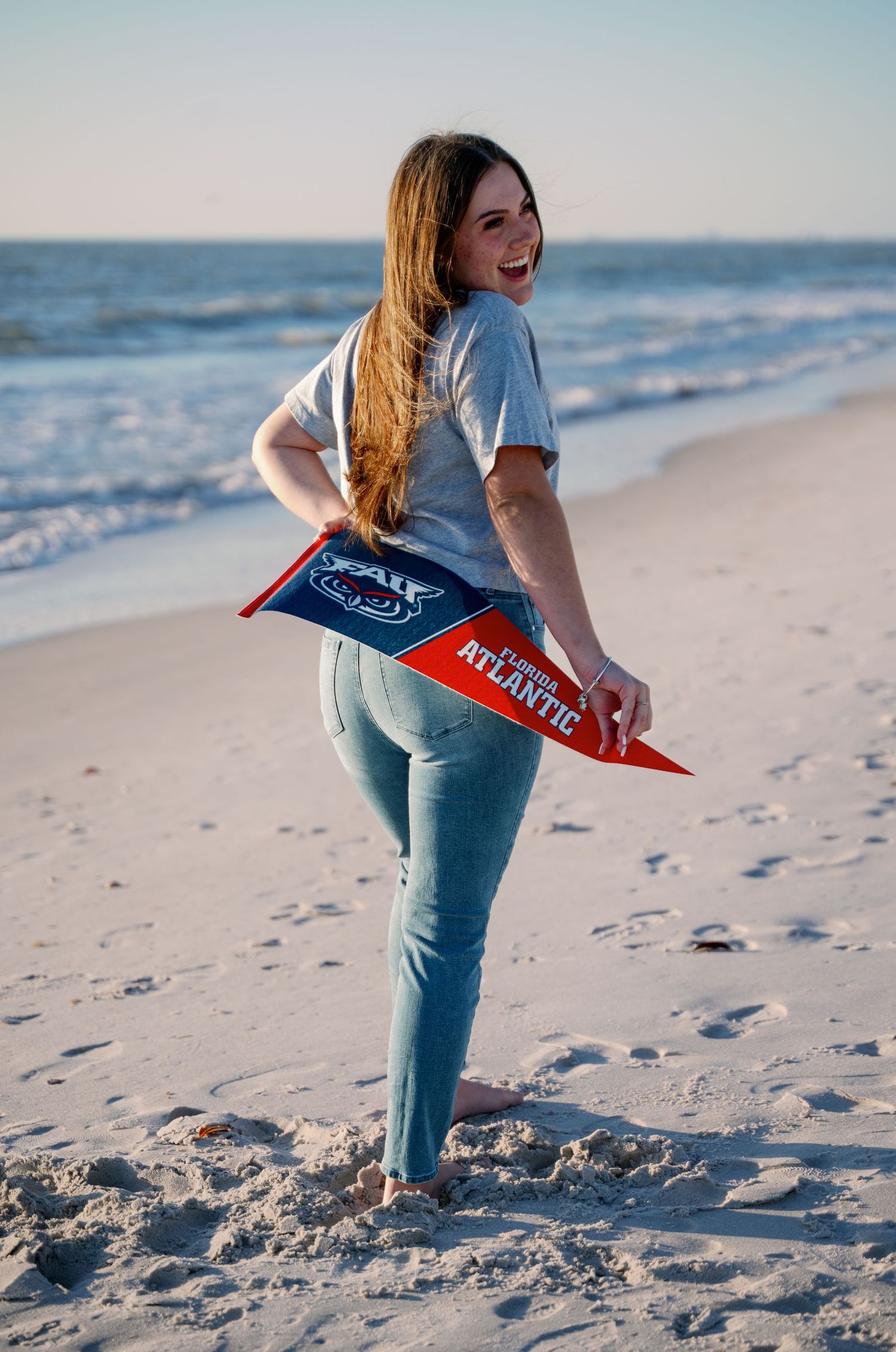 Playful beach photoshoot with FAU pennant flag against ocean backdrop.