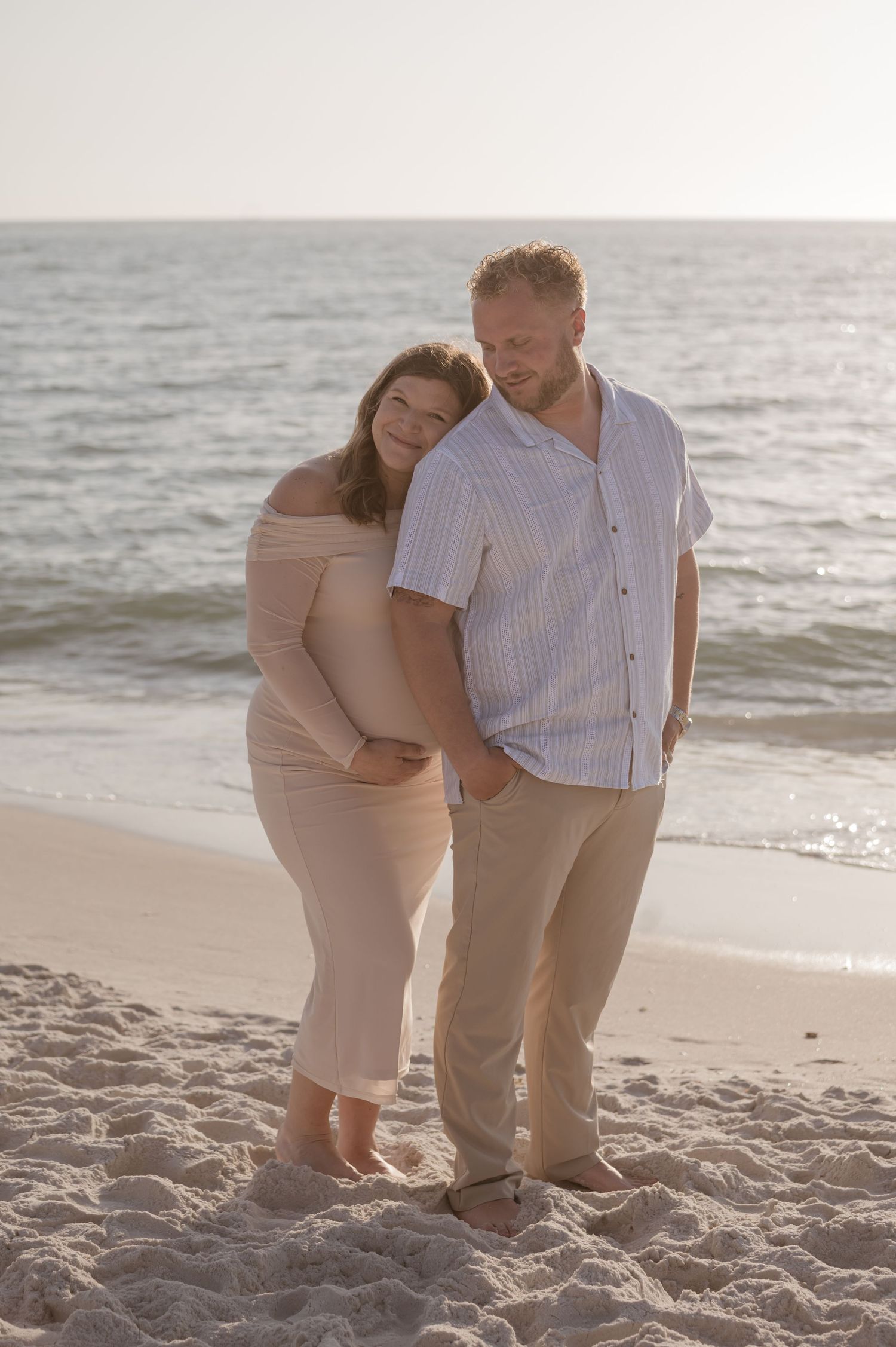 Expectant couple sharing tender moment on beach at sunset.
