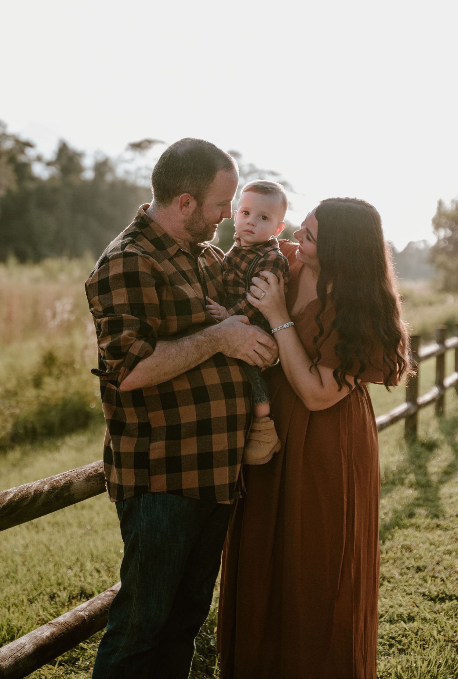 Outdoor family portrait session in a rustic field with warm sunset lighting.