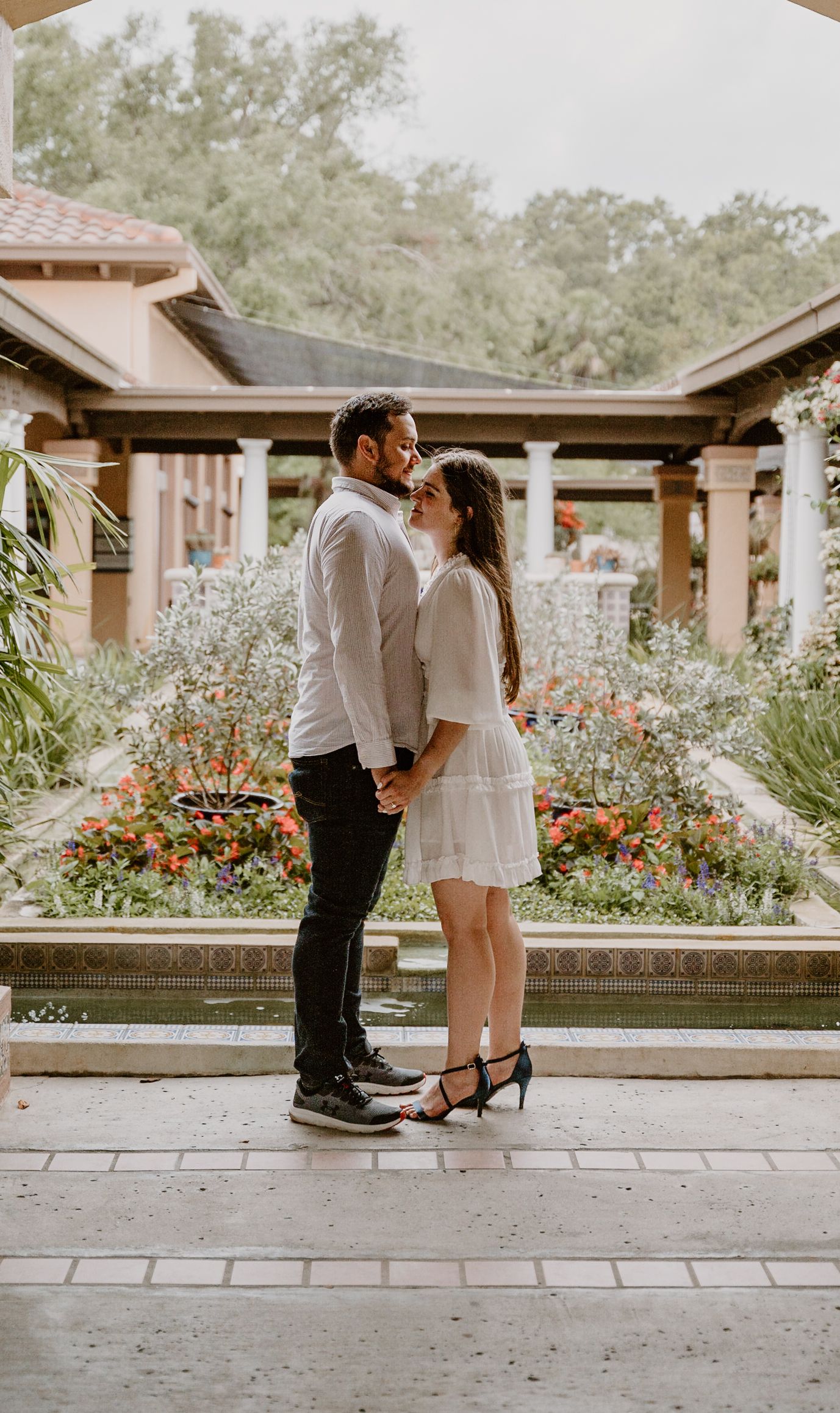 Couple sharing an intimate moment in a garden gazebo surrounded by blooming flowers.