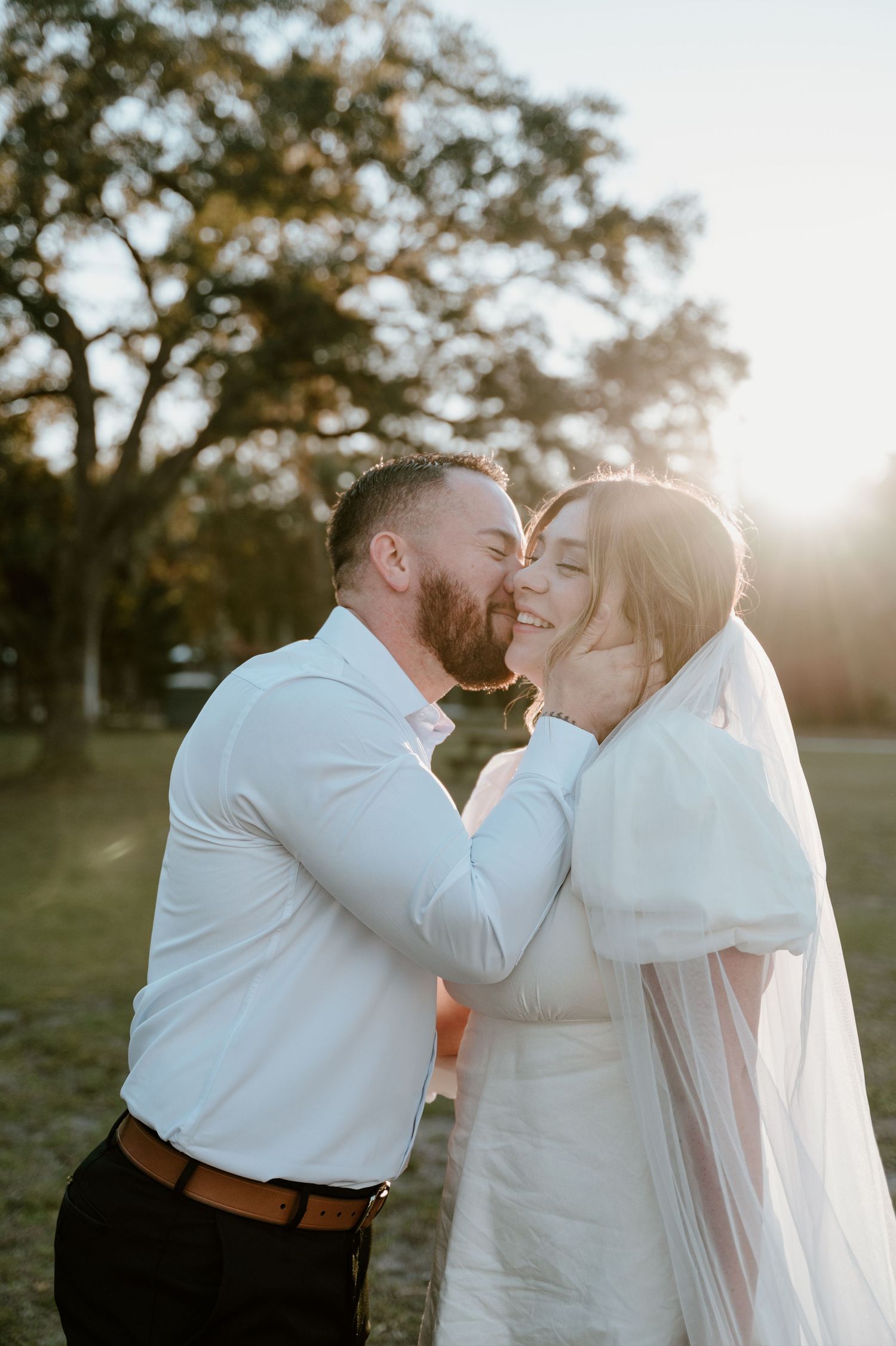 Newlywed couple sharing an intimate moment at sunset in a park setting with trees in the background.