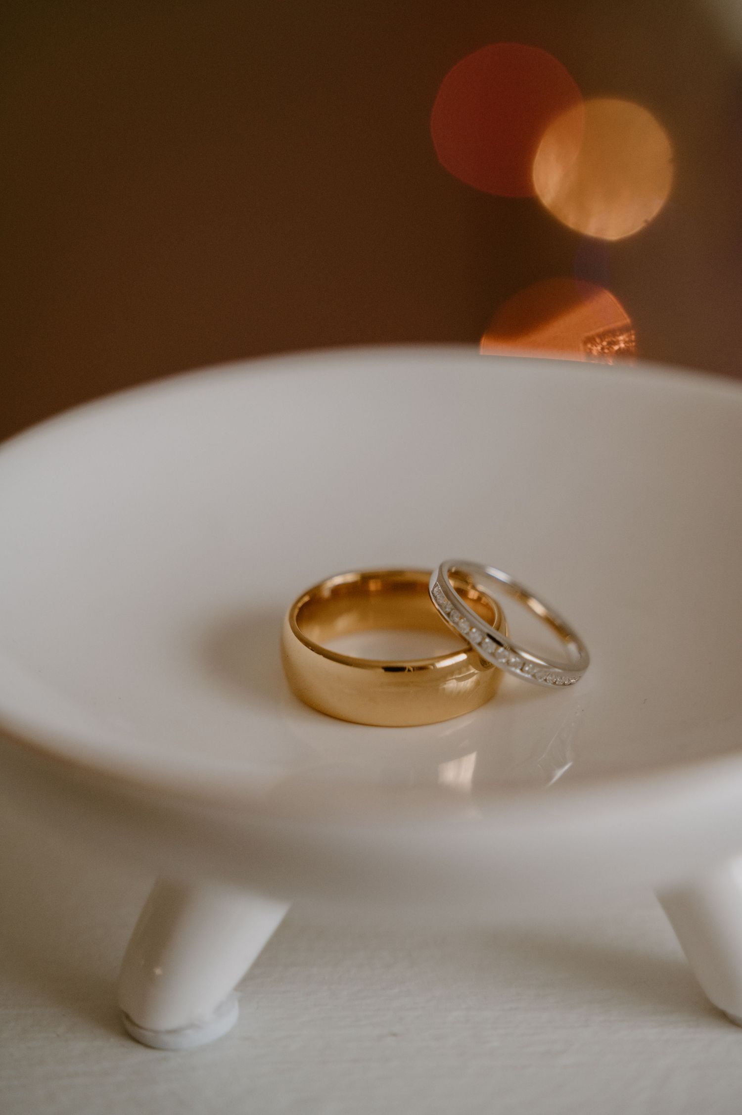 Wedding rings displayed on white surface with soft bokeh lighting effects.