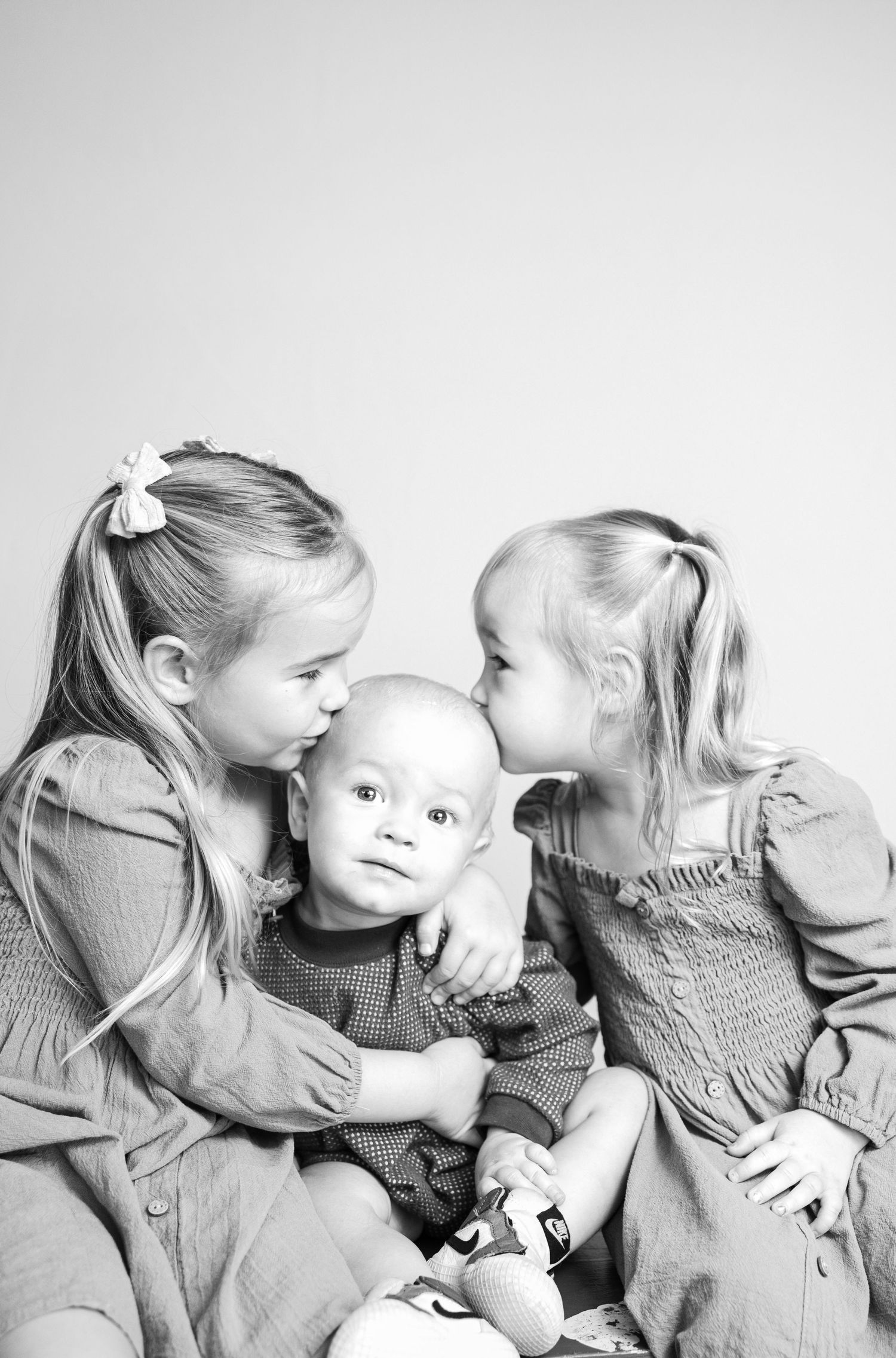 Three siblings in matching outfits share a tender black and white portrait moment together.