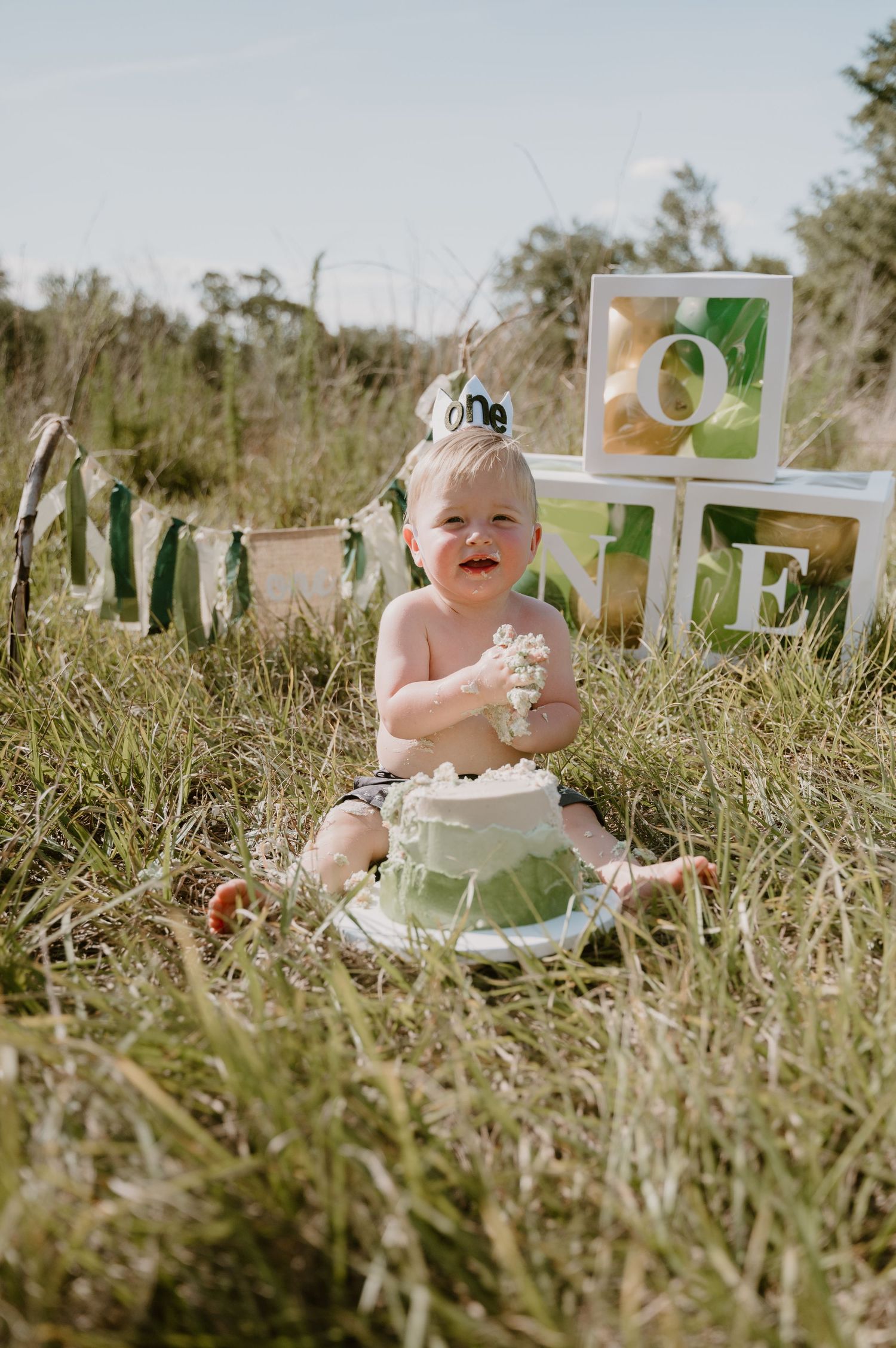 Baby's first birthday cake smash photo session outdoors with green and white decorations.