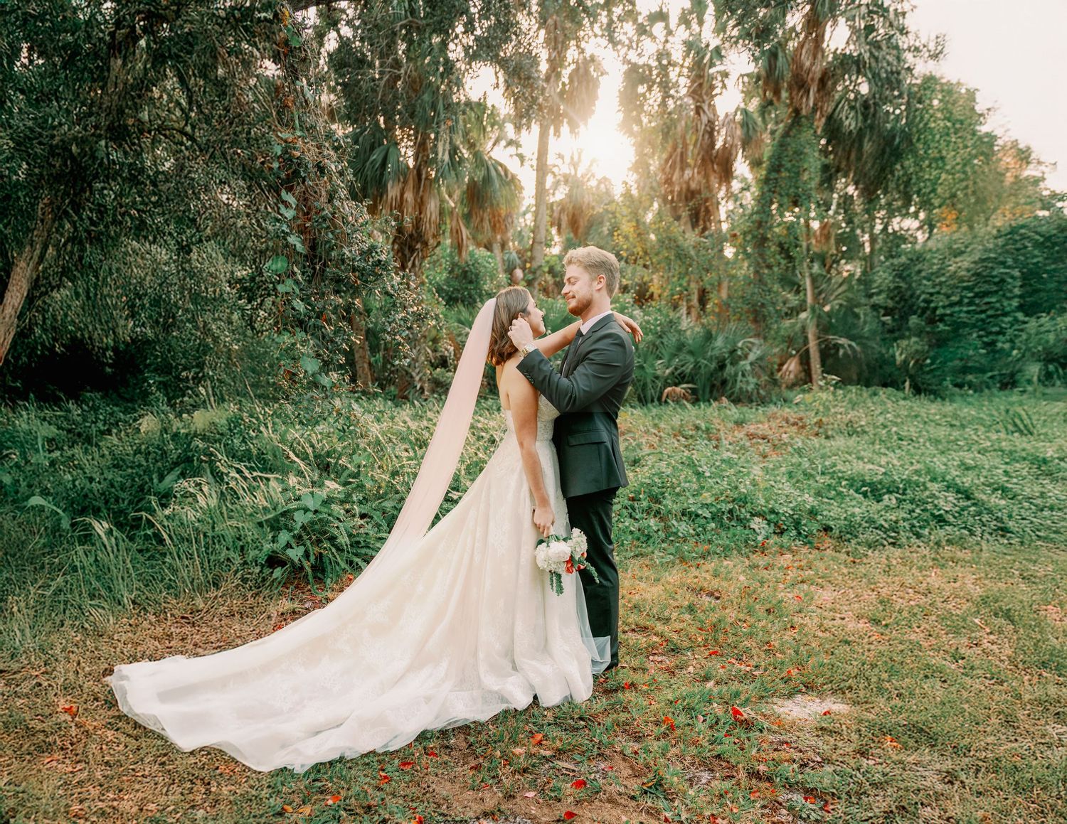 Wedding couple poses in lush garden setting during golden hour.