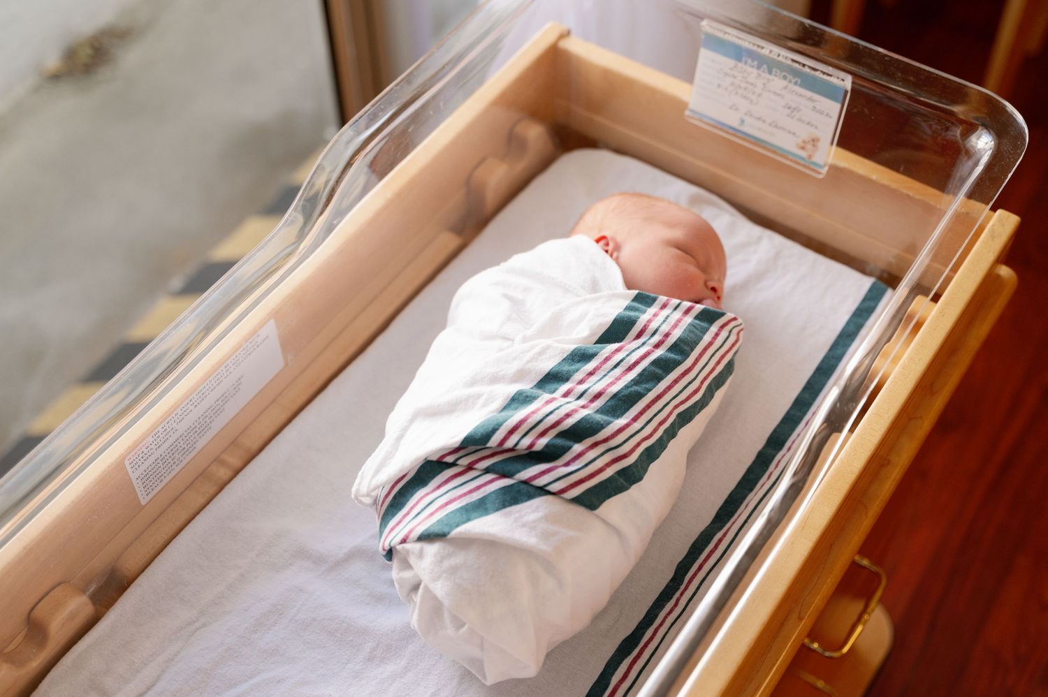 Newborn baby sleeping peacefully in a hospital bassinet with striped blanket and monitoring equipment.