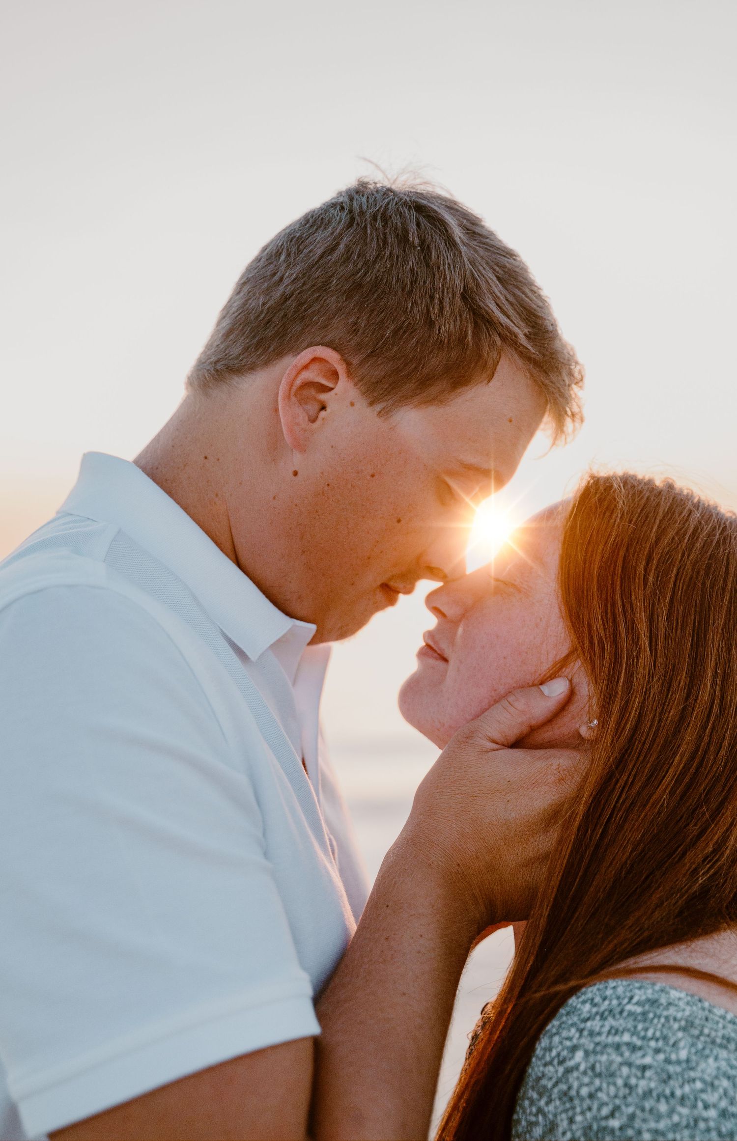 Couple sharing intimate moment as sunlight streams between them at sunset.