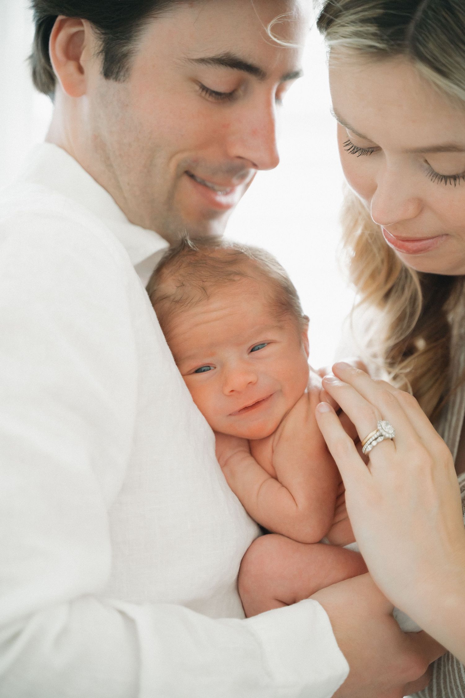 New parents holding their newborn baby while showing off engagement ring.