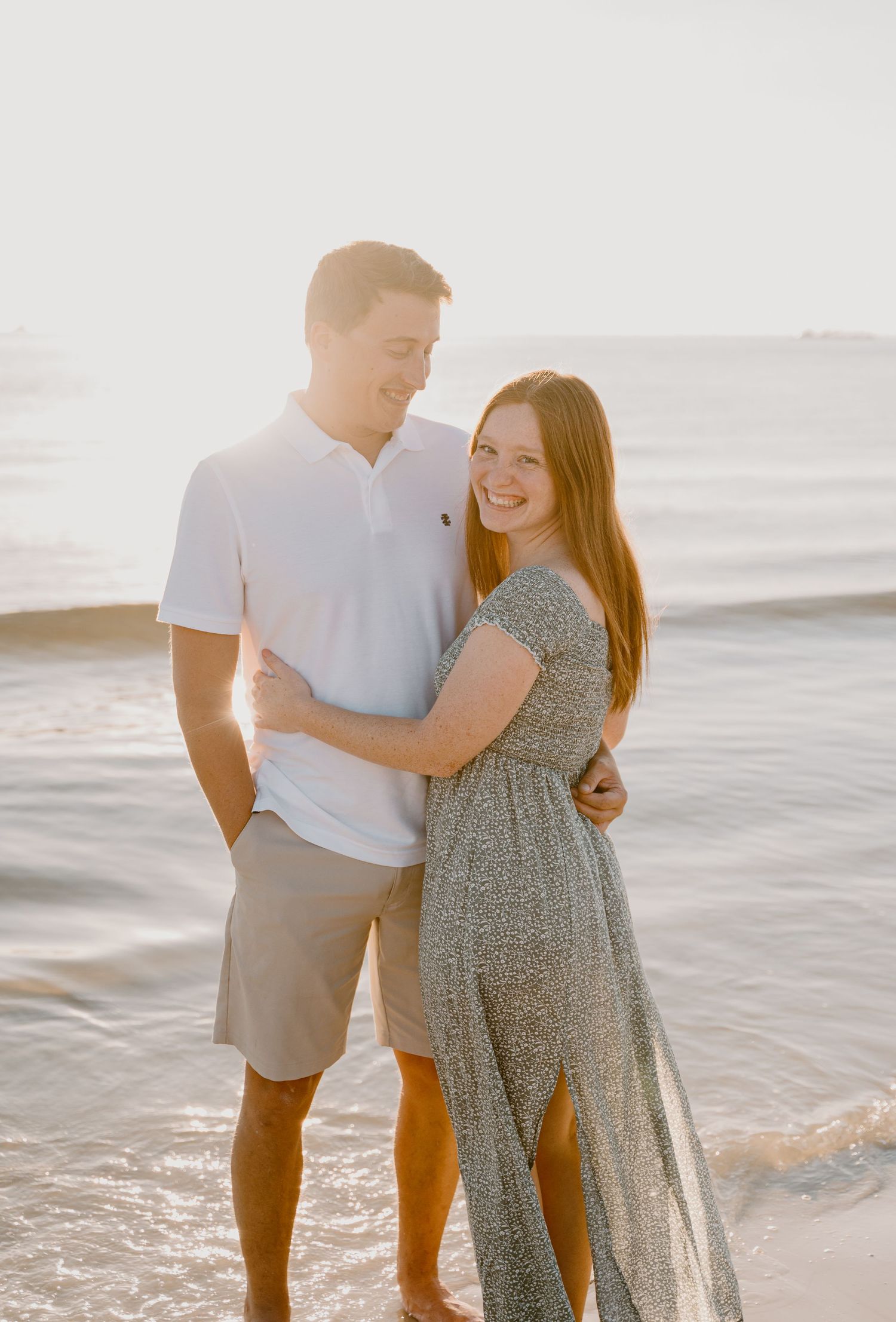 Couple embracing on beach during sunset with ocean waves in background.