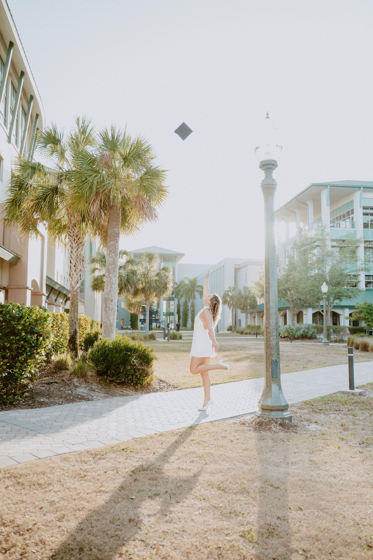 A person in a white dress poses near palm trees and beach condos during golden hour.