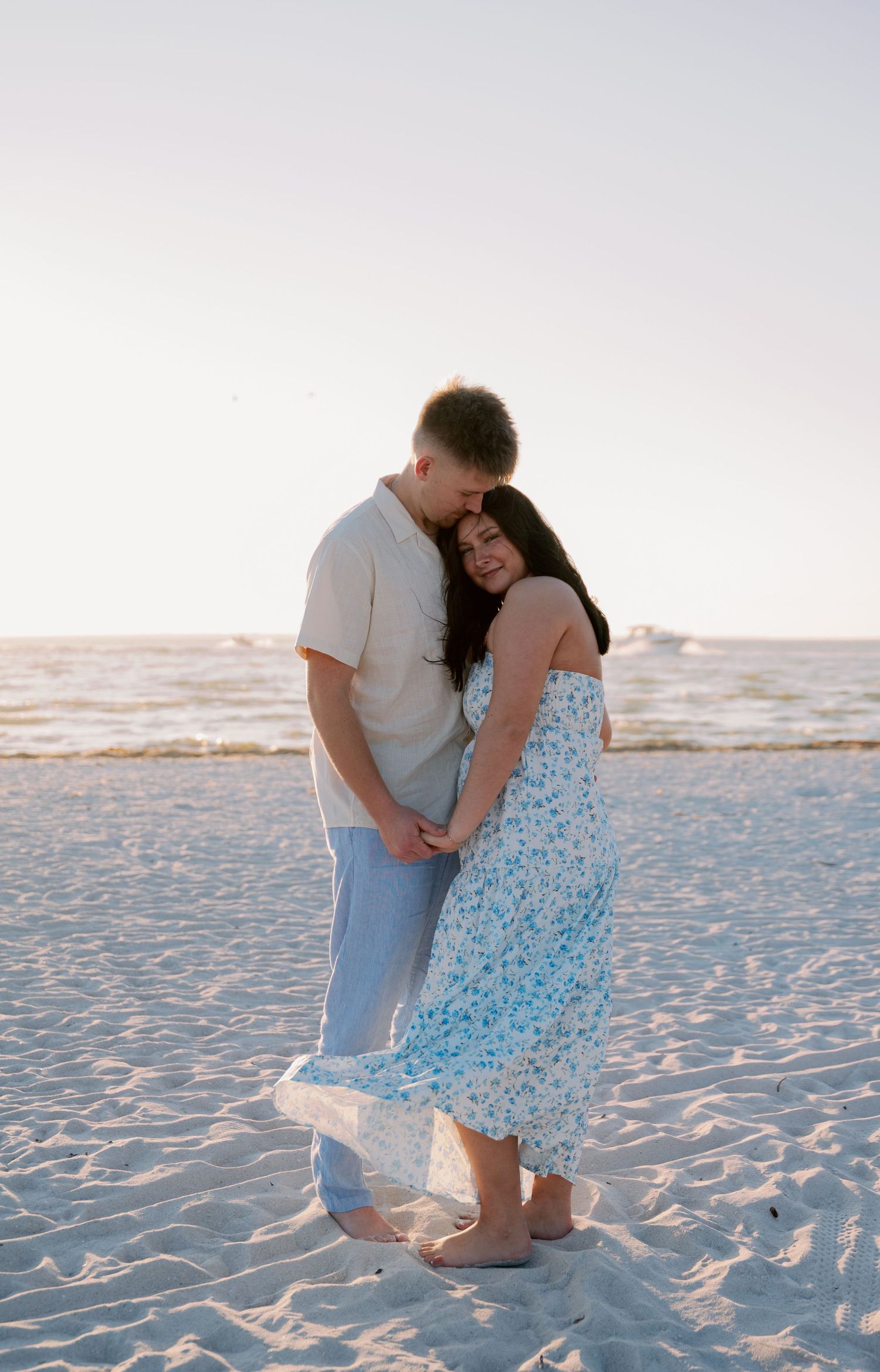 Couple shares romantic moment on sandy beach during sunset engagement session.