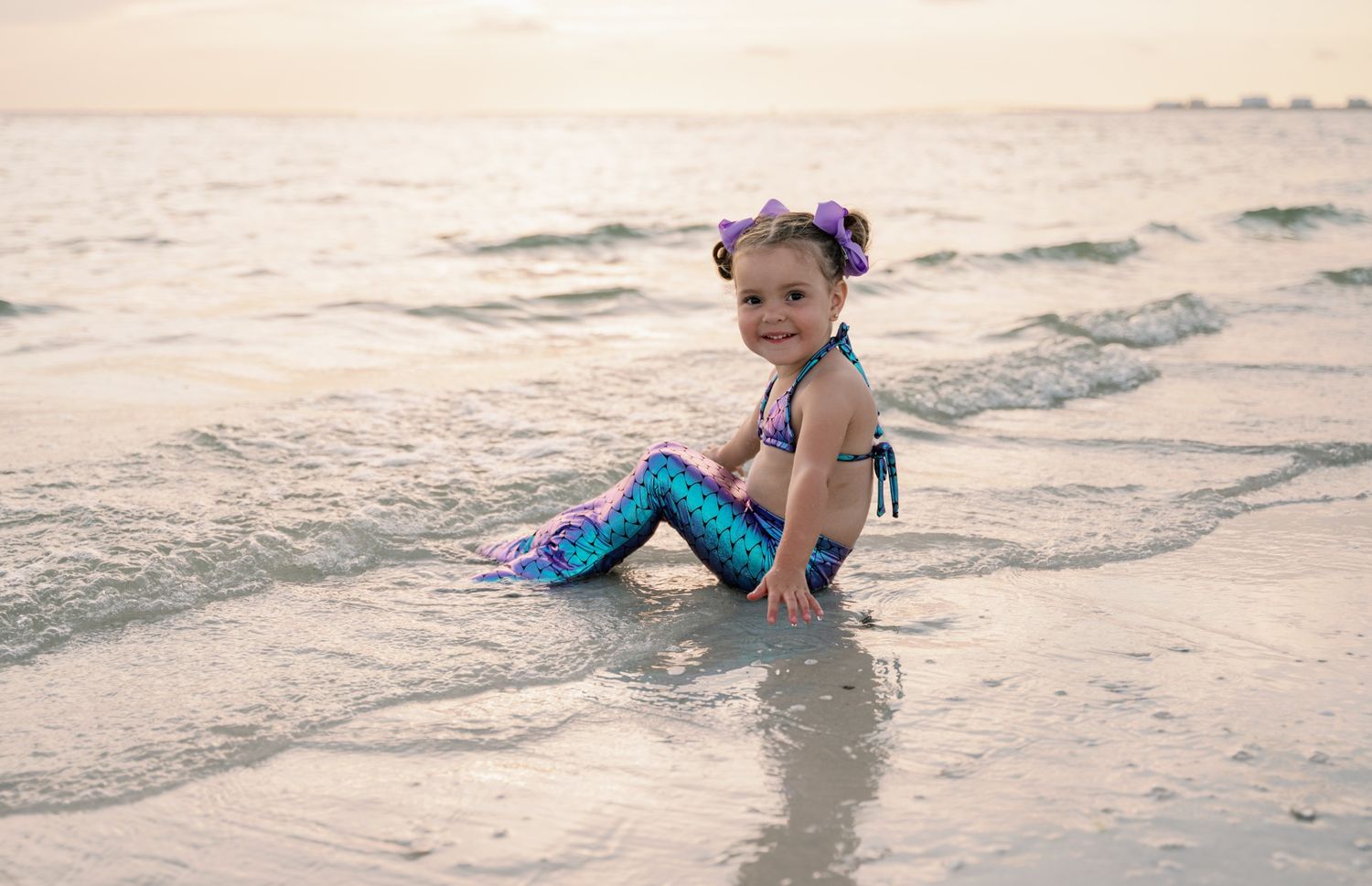A series of photos showing a small child playing and splashing in shallow beach waves at sunset.