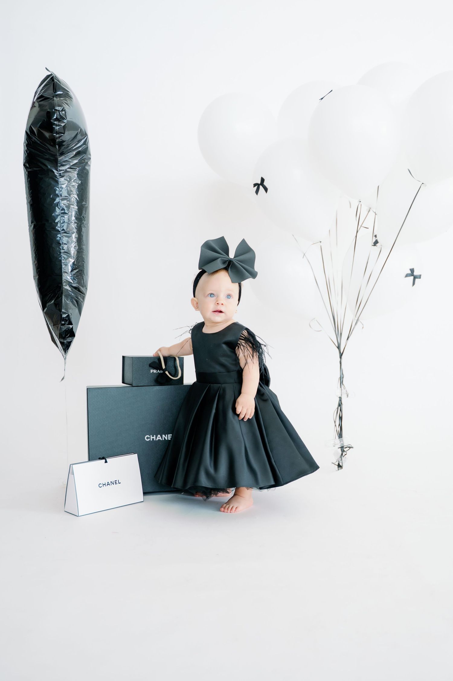 Minimalist fashion photography with black dress and Chanel shopping bags in white studio setting.