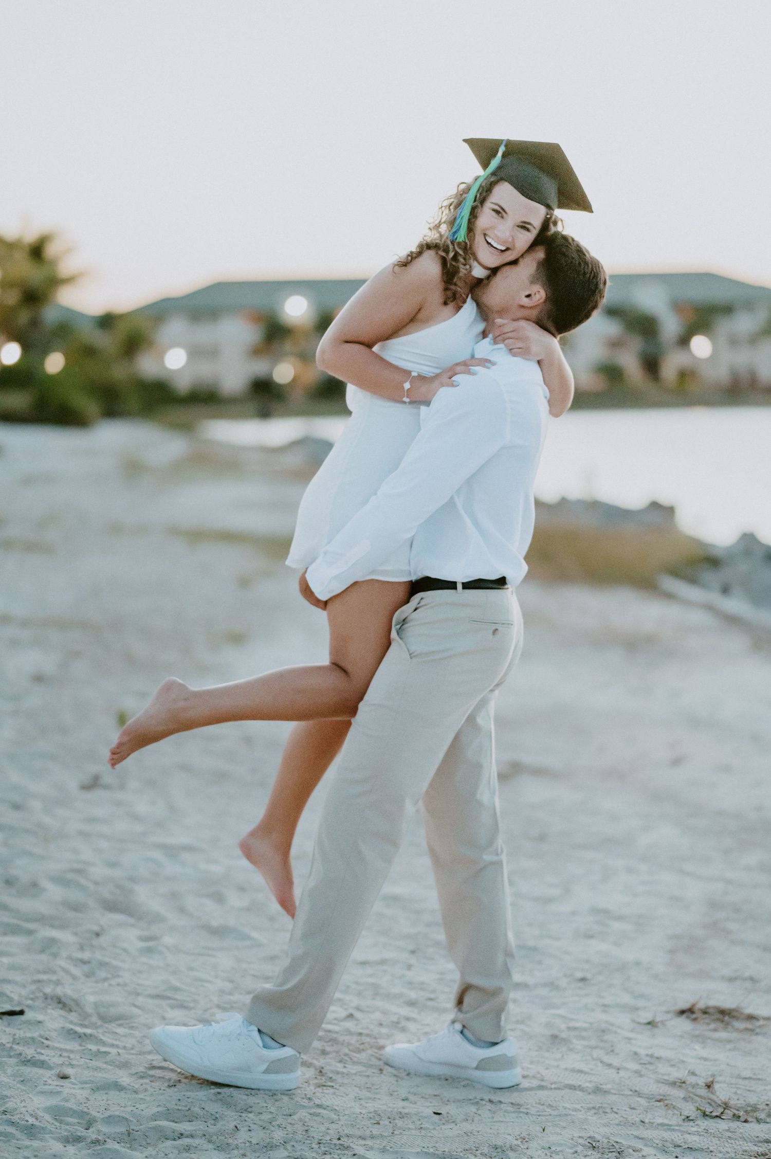A celebratory graduation moment captured on the beach at sunset.