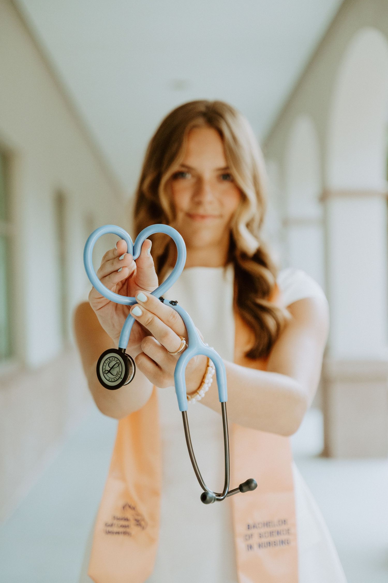 A healthcare professional holds up a stethoscope in a bright hallway.
