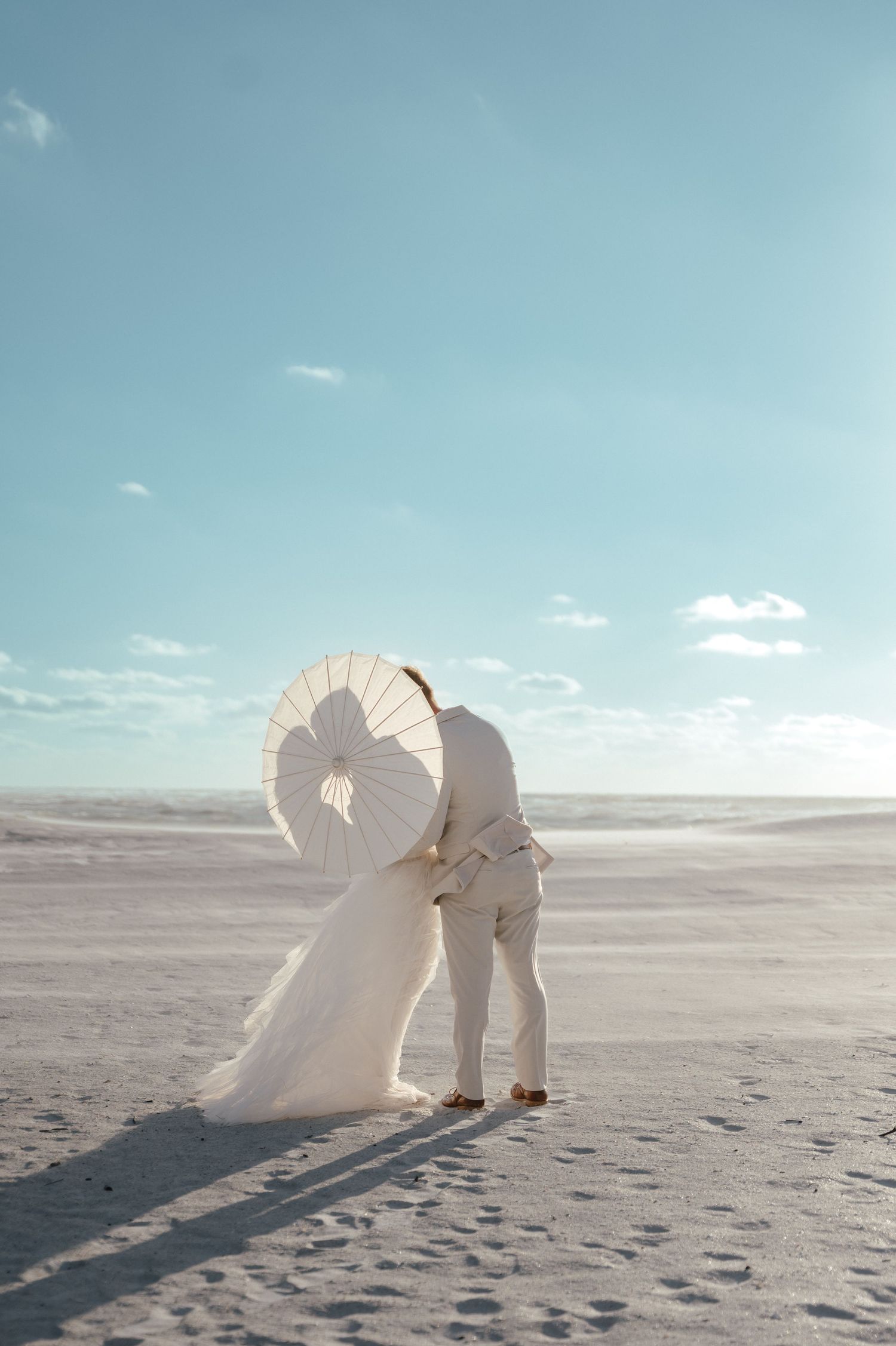 Artistic beach photography with white parasol casting long shadows on sand.