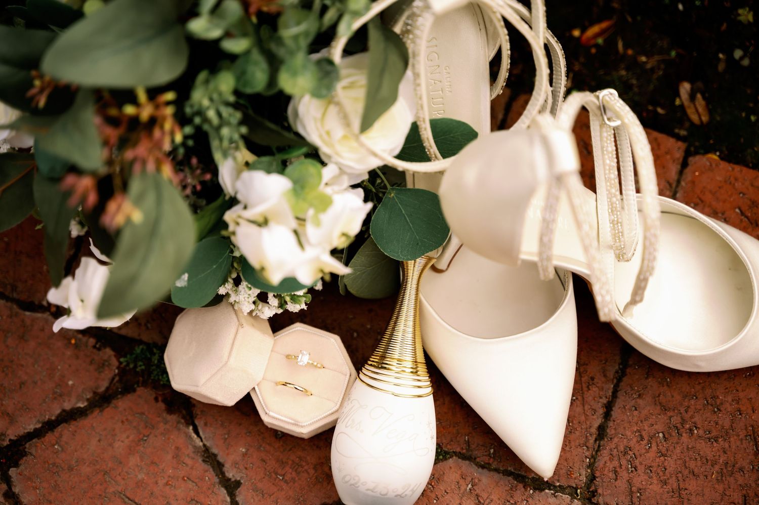 White bridal shoes and accessories arranged with floral decorations on brick surface.