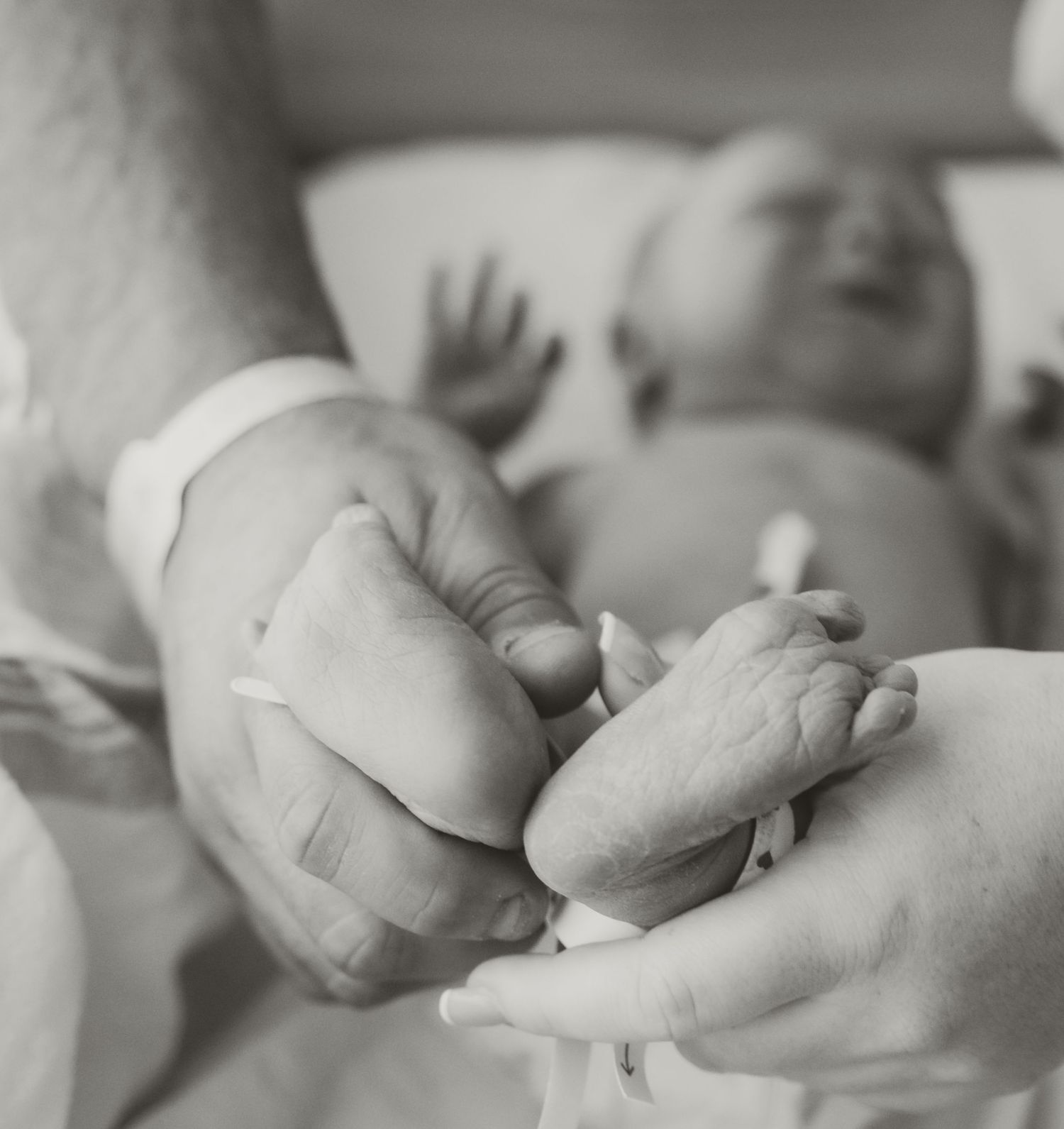 Close-up black and white image of a sleeping newborn baby's hands and face.