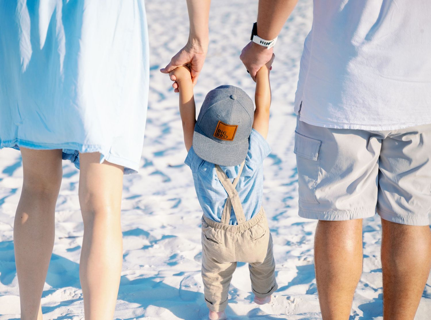 Close-up of hands holding a blue baseball cap on sandy beach.