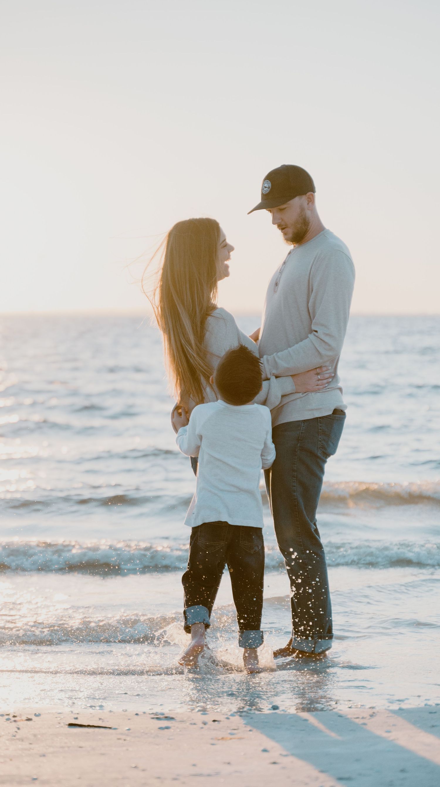 Couple splashing in ocean waves during romantic beach photoshoot at sunset.