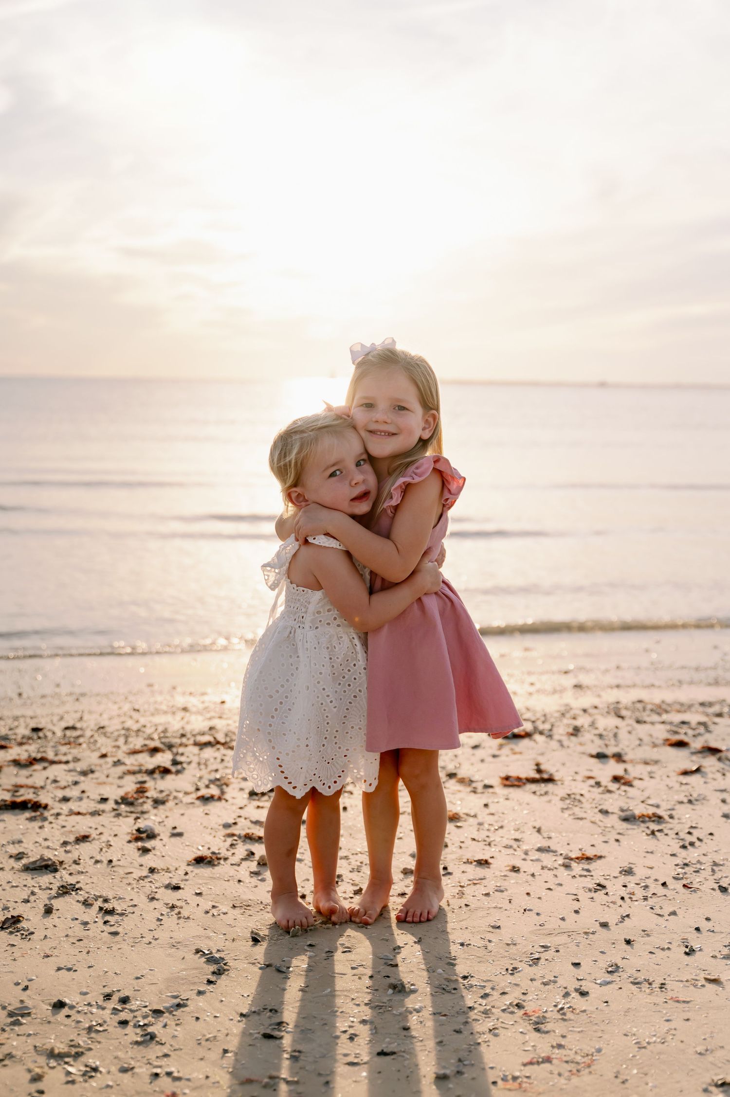 Young children in light dresses hugging and playing on a sunset beach.