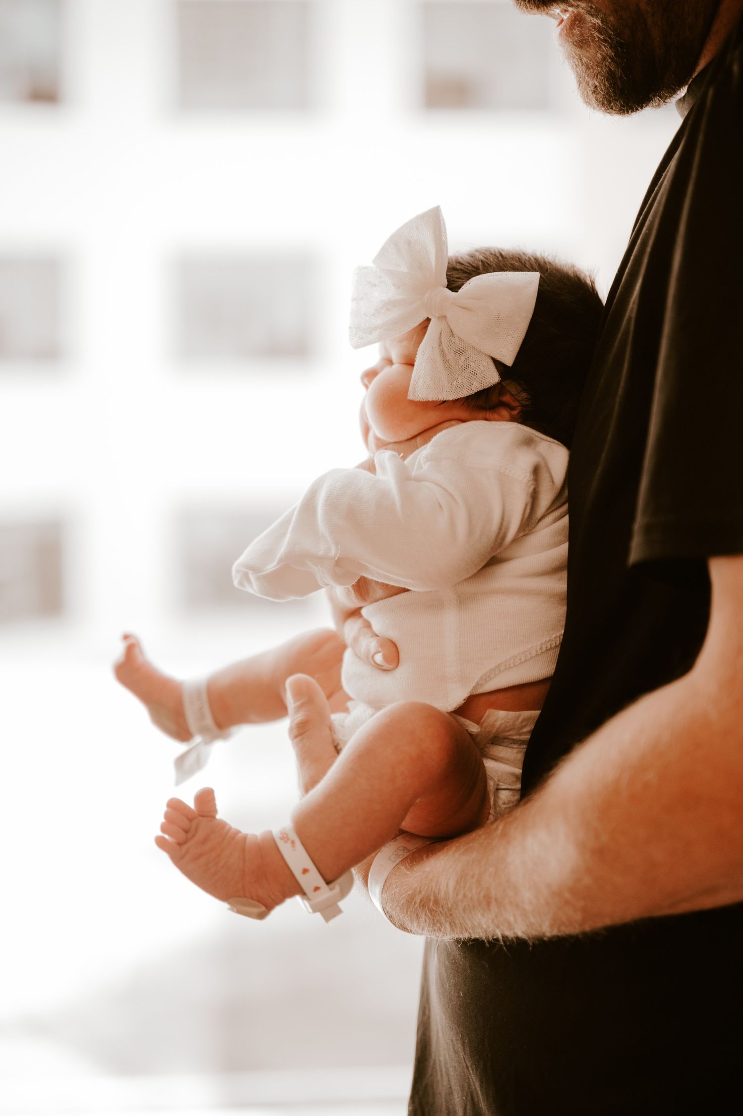 Person holding a small baby dressed in white with a bow.