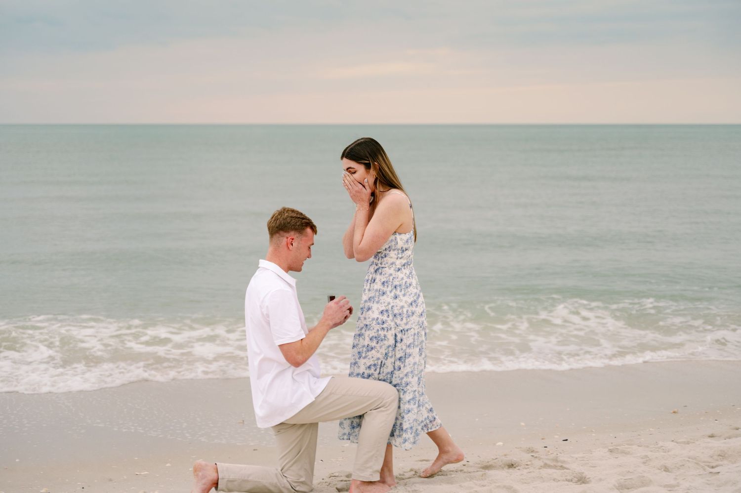 Beachside proposal scene with waves and sand in the background.
