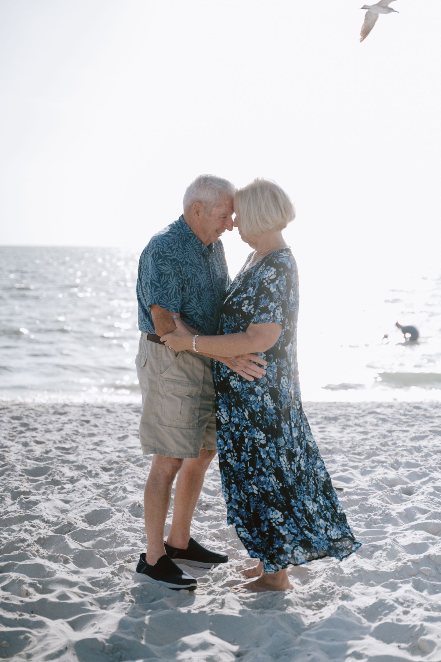Senior couple dancing together on a sandy beach with seagulls flying overhead.