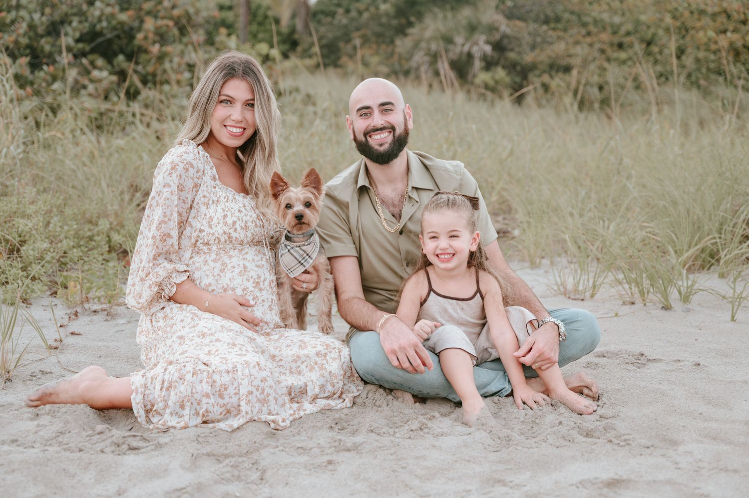 Family sitting together on sandy dunes during golden hour photo session.