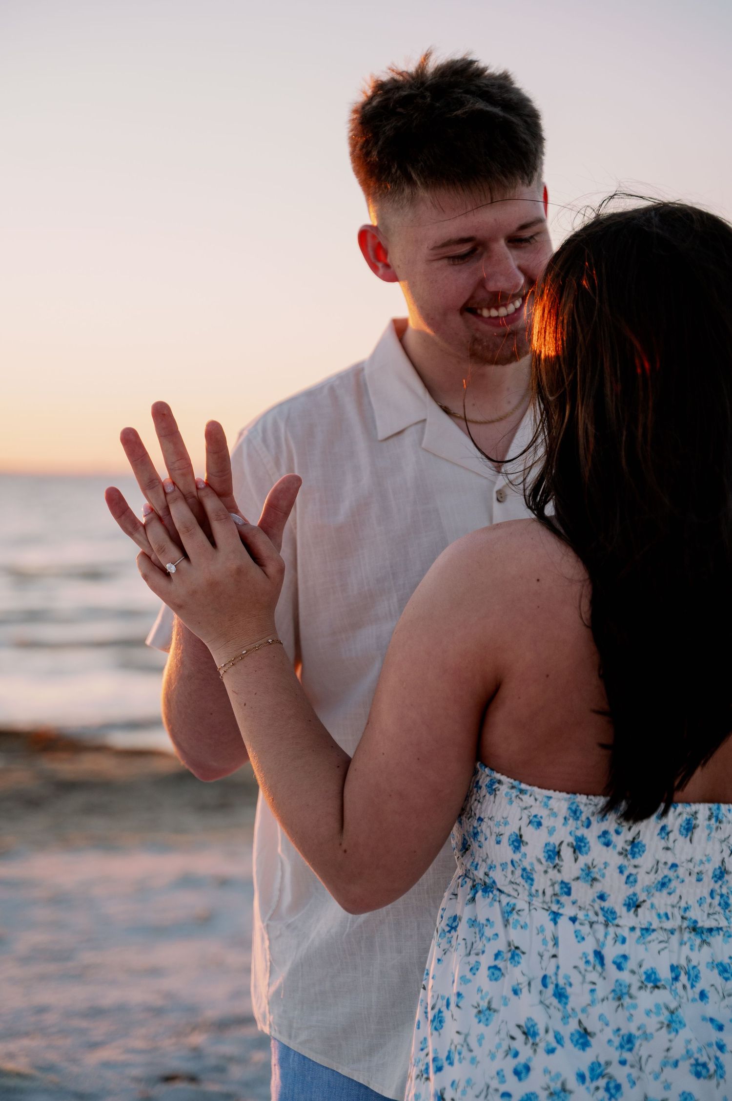 Happy couple showing engagement ring on beach during sunset photoshoot.
