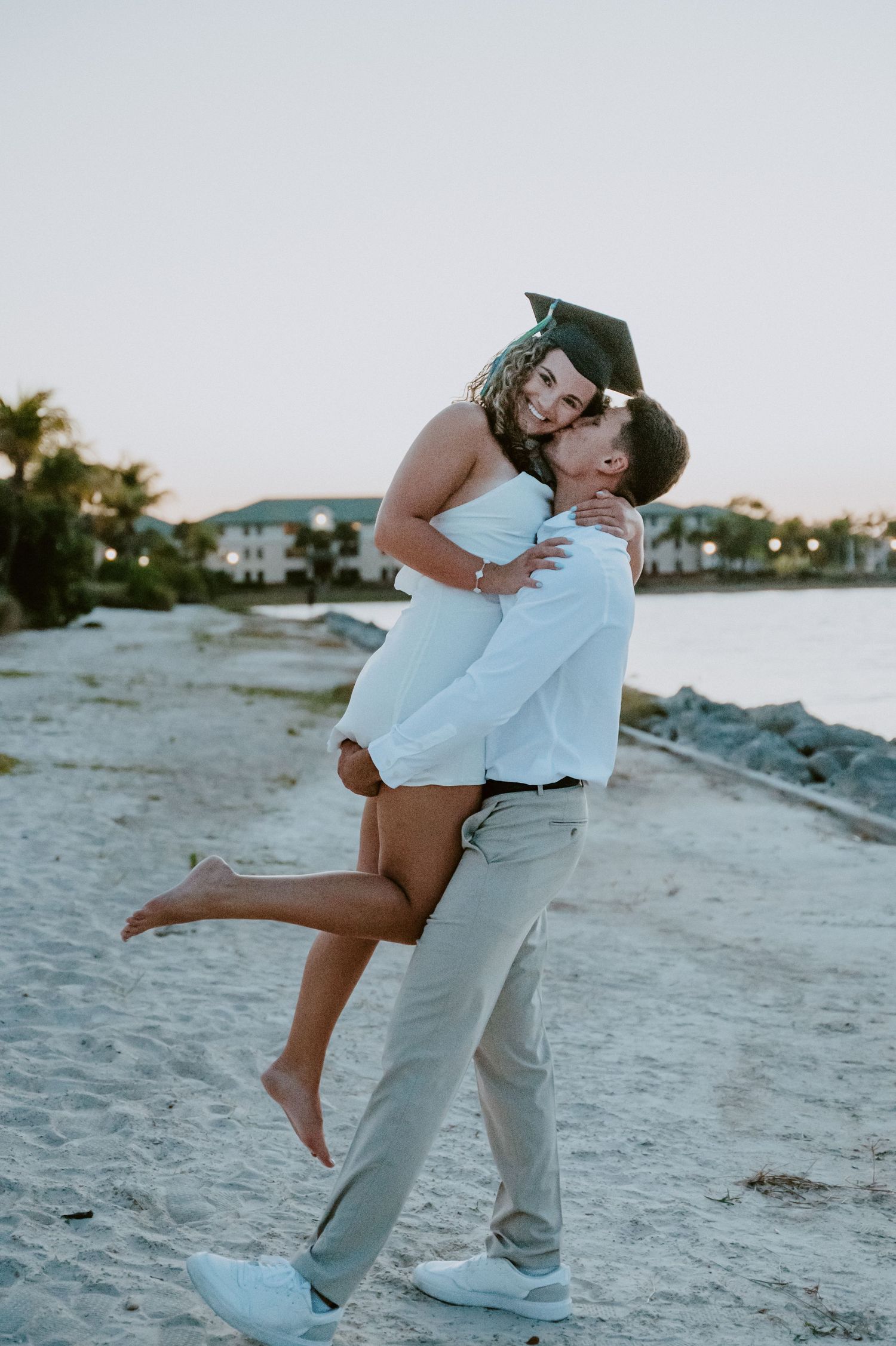 Romantic beach photoshoot with couple in light blue and white outfits at sunset.