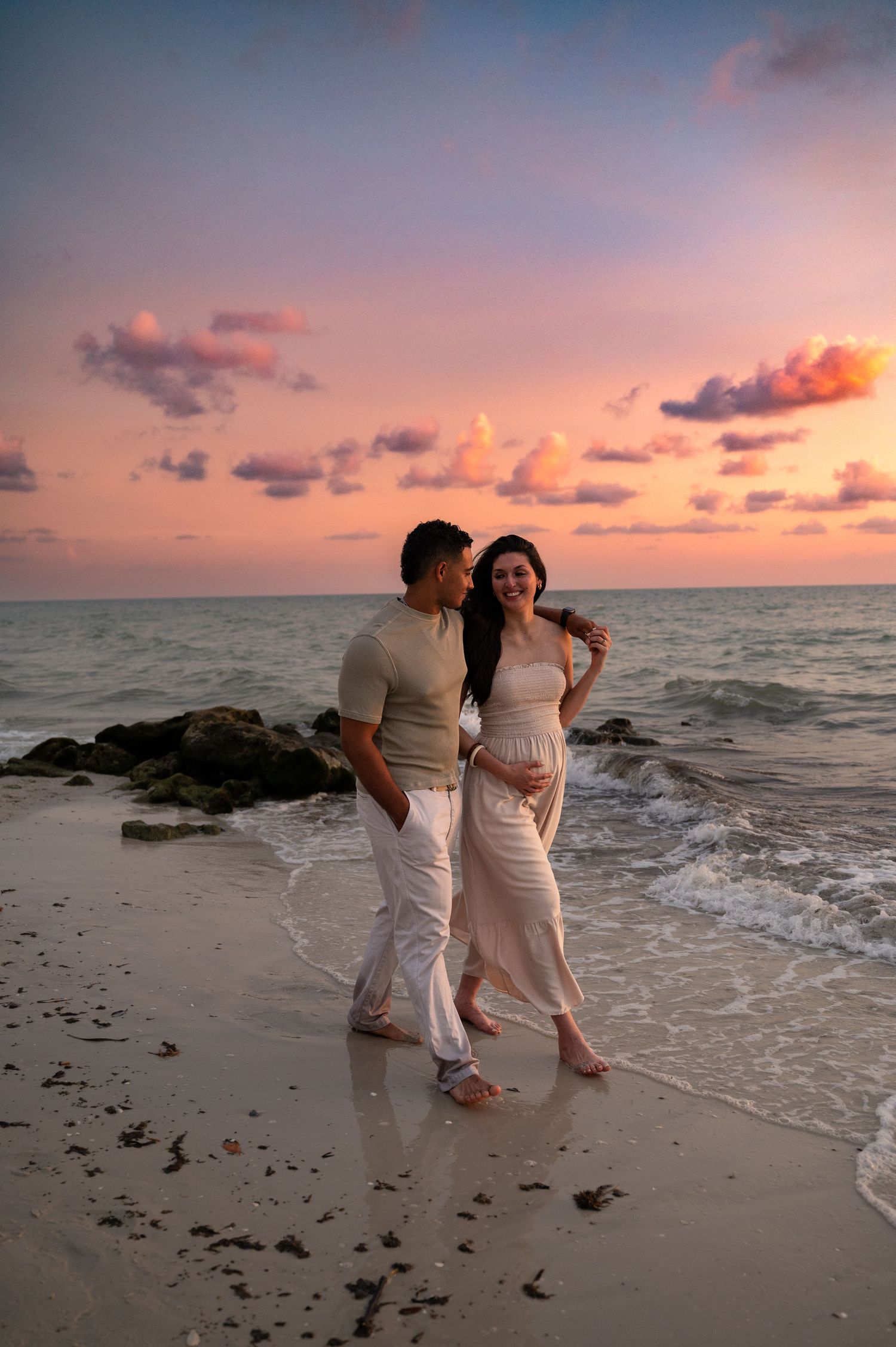 Couple walking along beach shoreline during vibrant sunset.