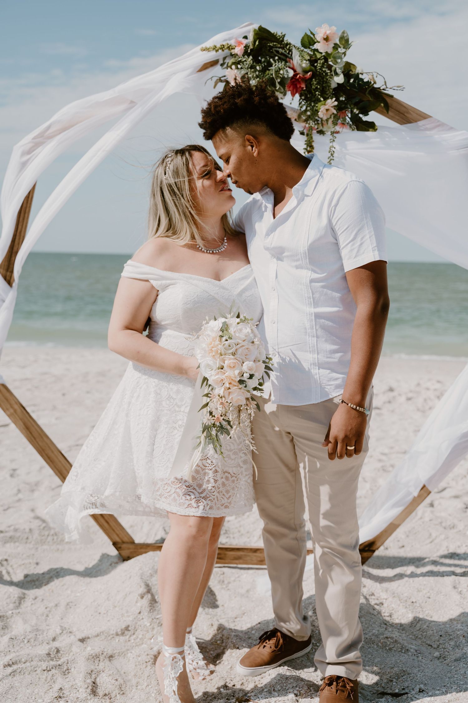 Romantic beach wedding photoshoot with flowing veil and white floral bouquet.