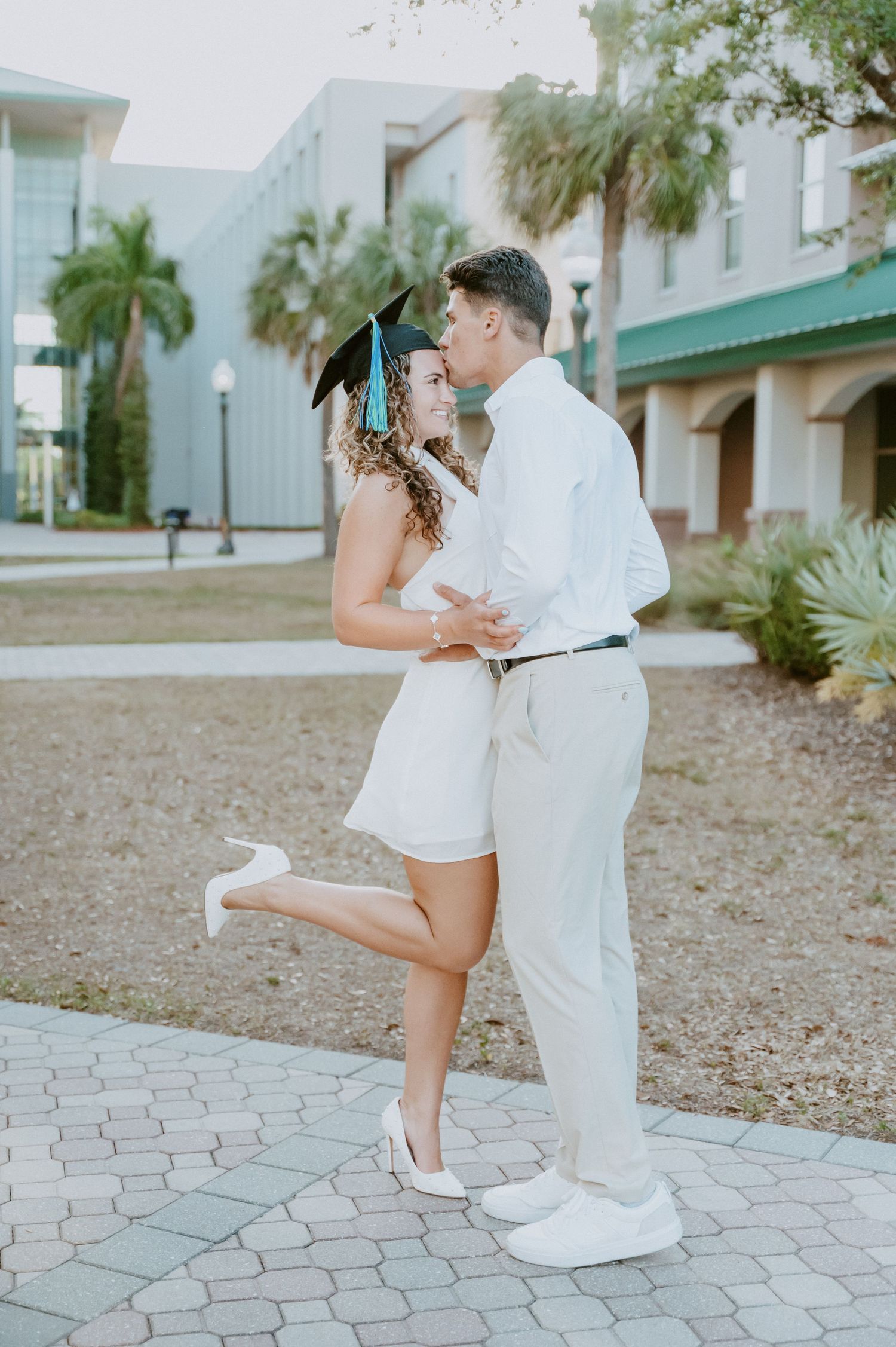 Couple in white outfits sharing playful moments on brick paved courtyard.