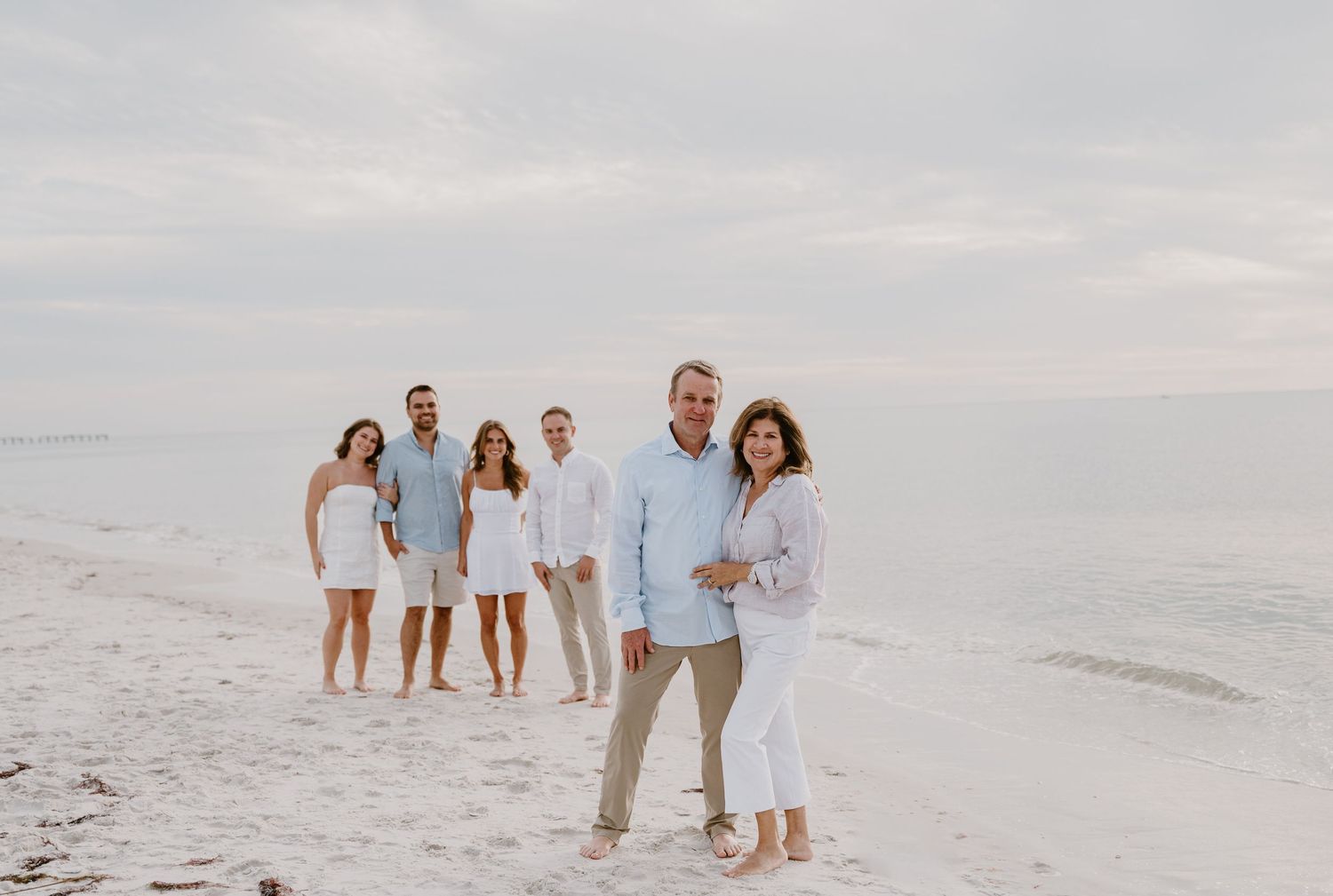 Extended family in coordinated white and blue outfits poses for beach portrait.
