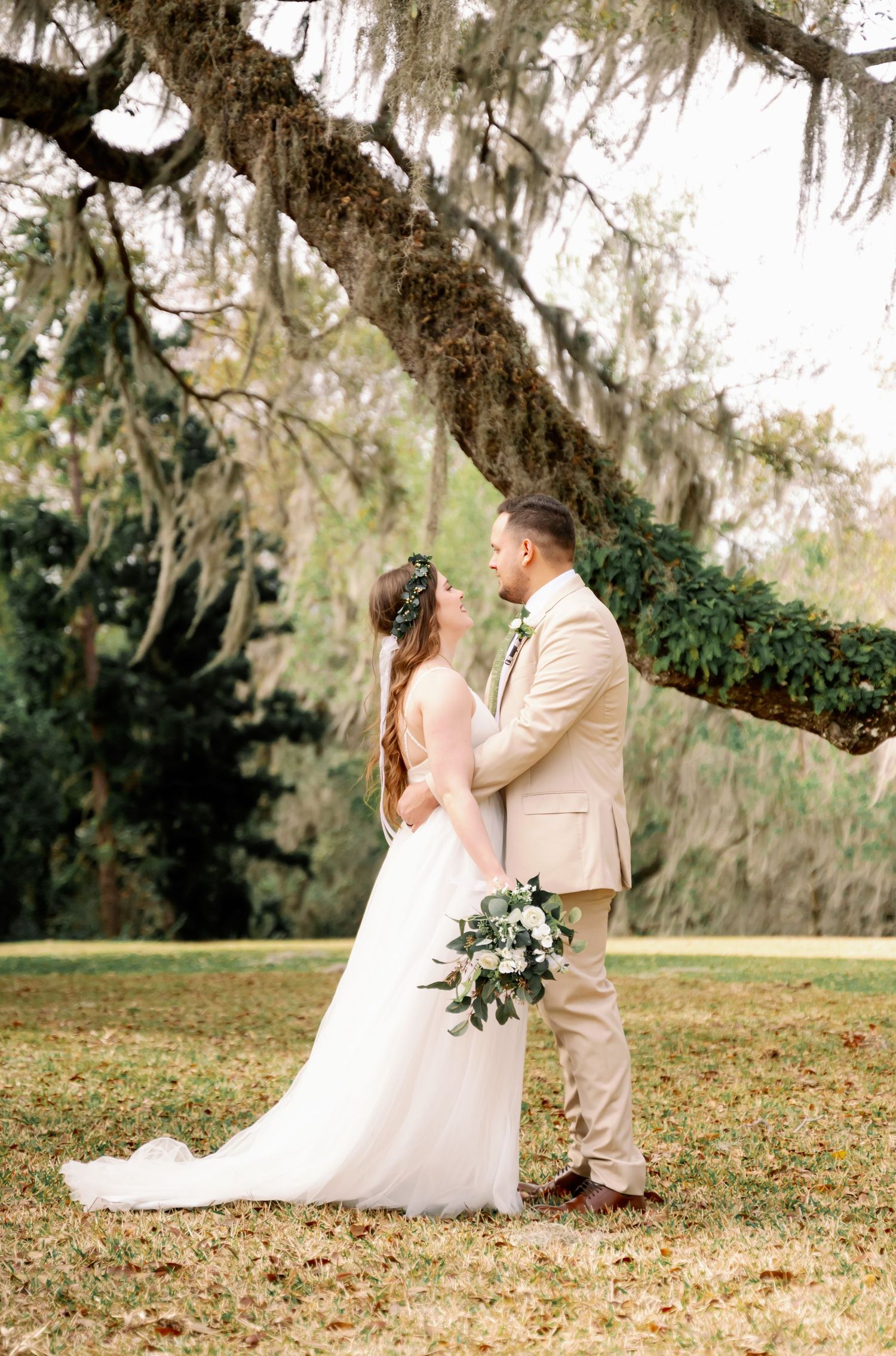 Wedding couple poses under Spanish moss trees in romantic outdoor setting.