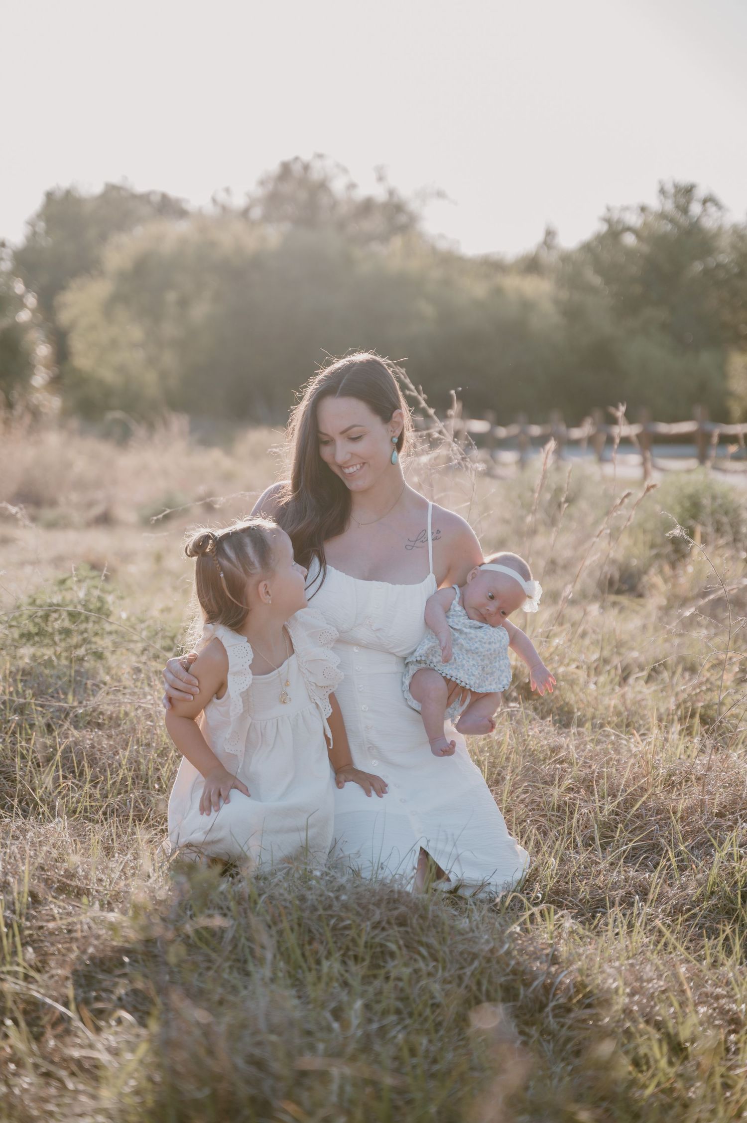 Mother in white dress sitting in field with children during golden hour.