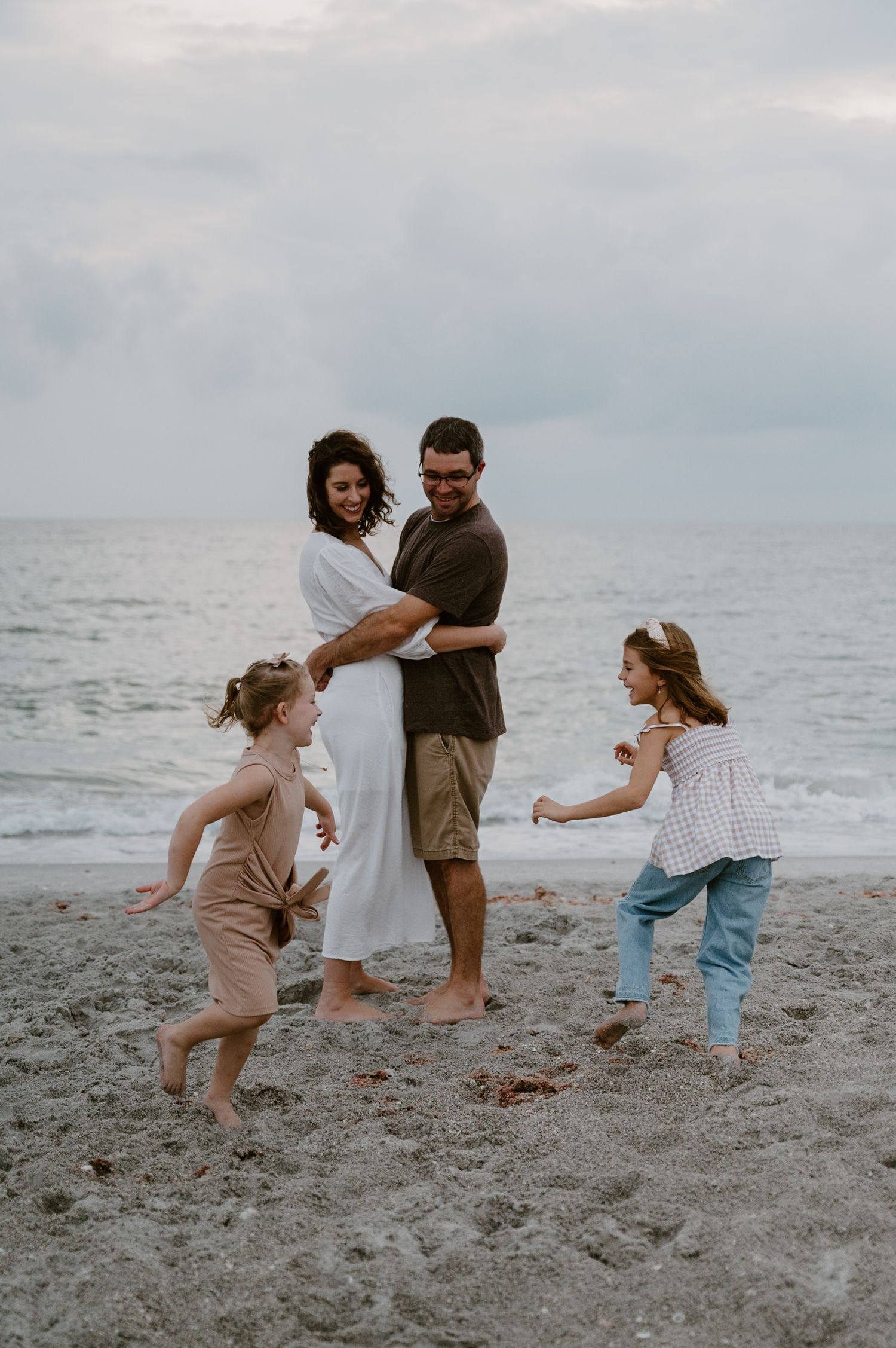 Family playing and jumping together on a grey sandy beach at dusk.