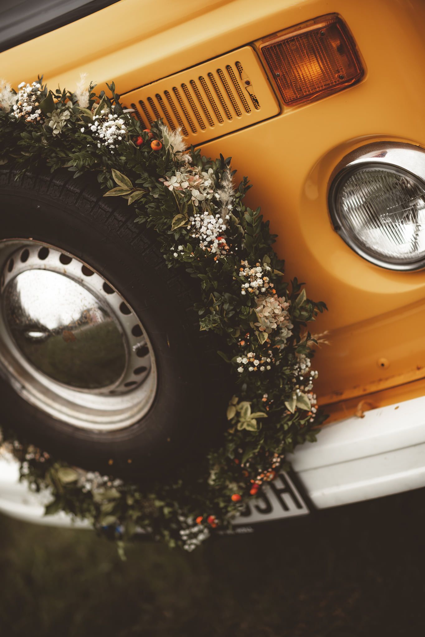 Close-up details of a classic yellow vintage car with decorative floral arrangements and headlights.