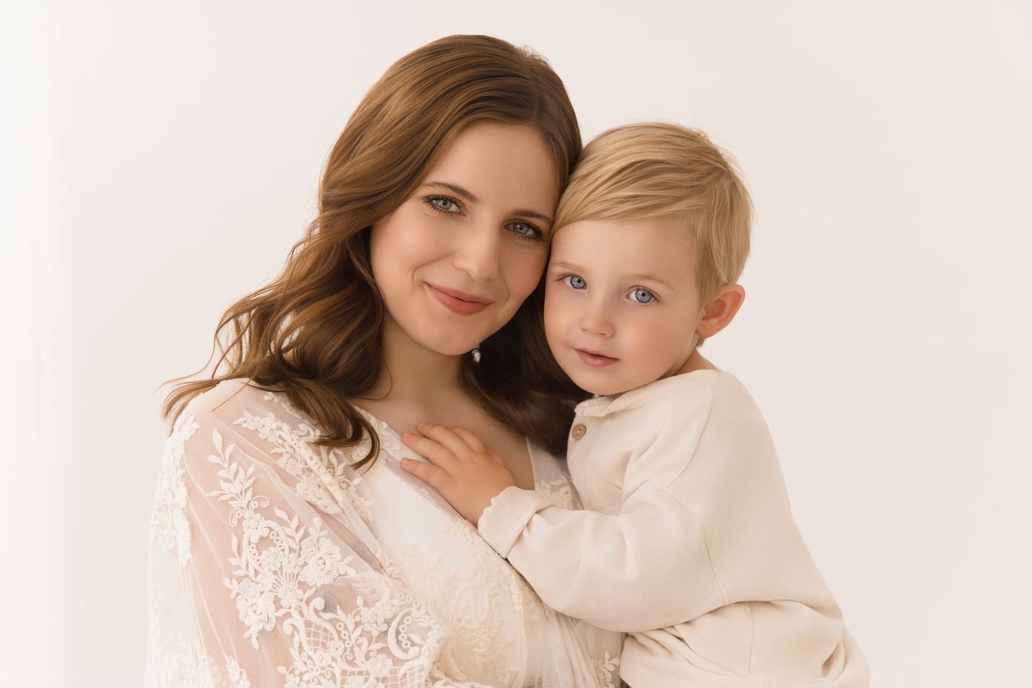 A mother and child in white lace outfits embrace lovingly in a soft, ethereal portrait series.