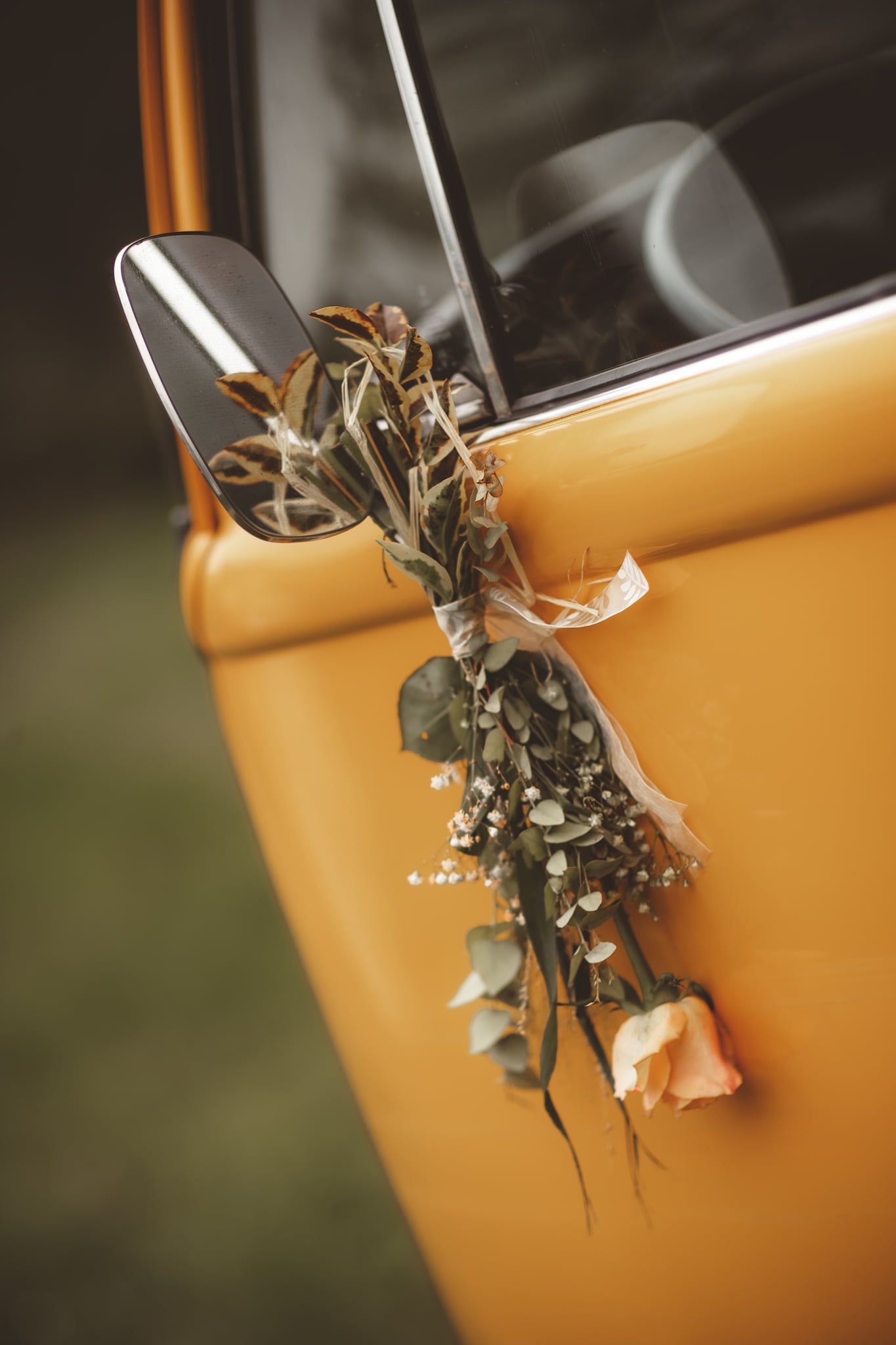 Dried floral arrangement decorating yellow vintage van door handle.