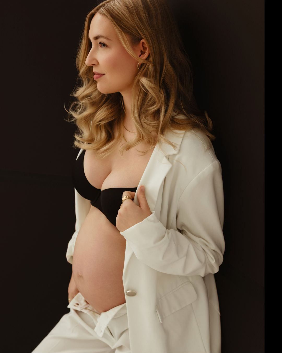 Artistic portrait against dark background featuring a white blazer and black undergarment with soft lighting.