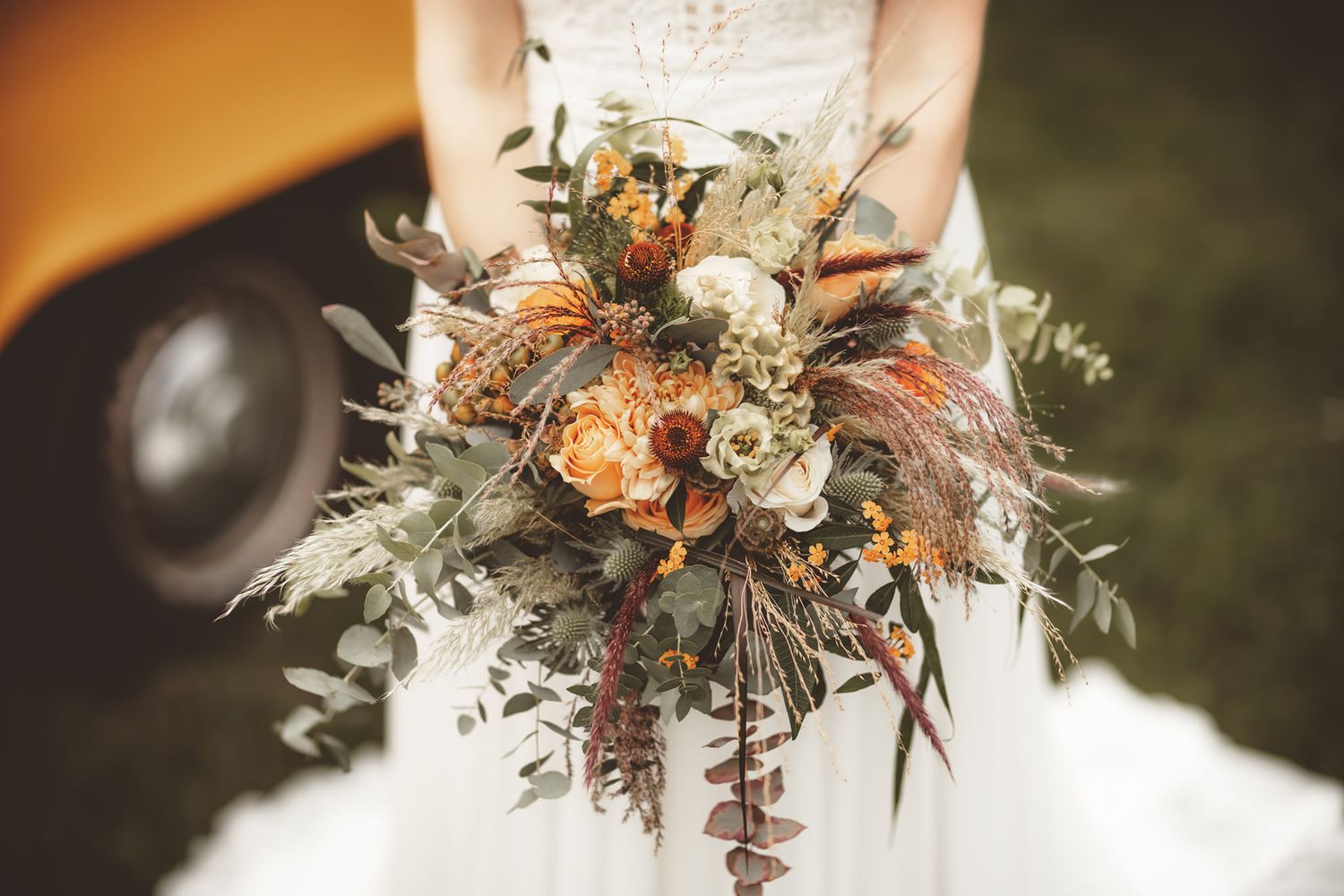Rustic autumn-inspired wedding bouquet with dried flowers and foliage in warm orange and neutral tones.